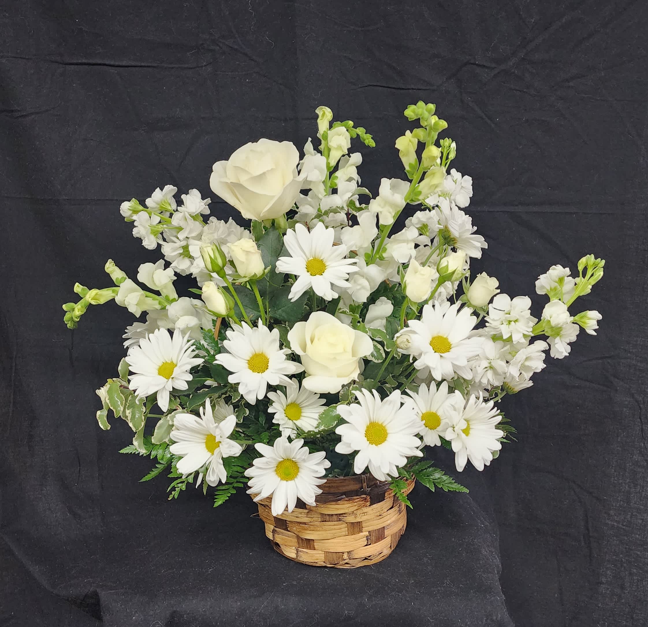 Remembrance - All white snapdragons, stock, roses and daisies arranged in a brown wicker handled basket convey your sympathy and comfort in remembering the loss loved one. 