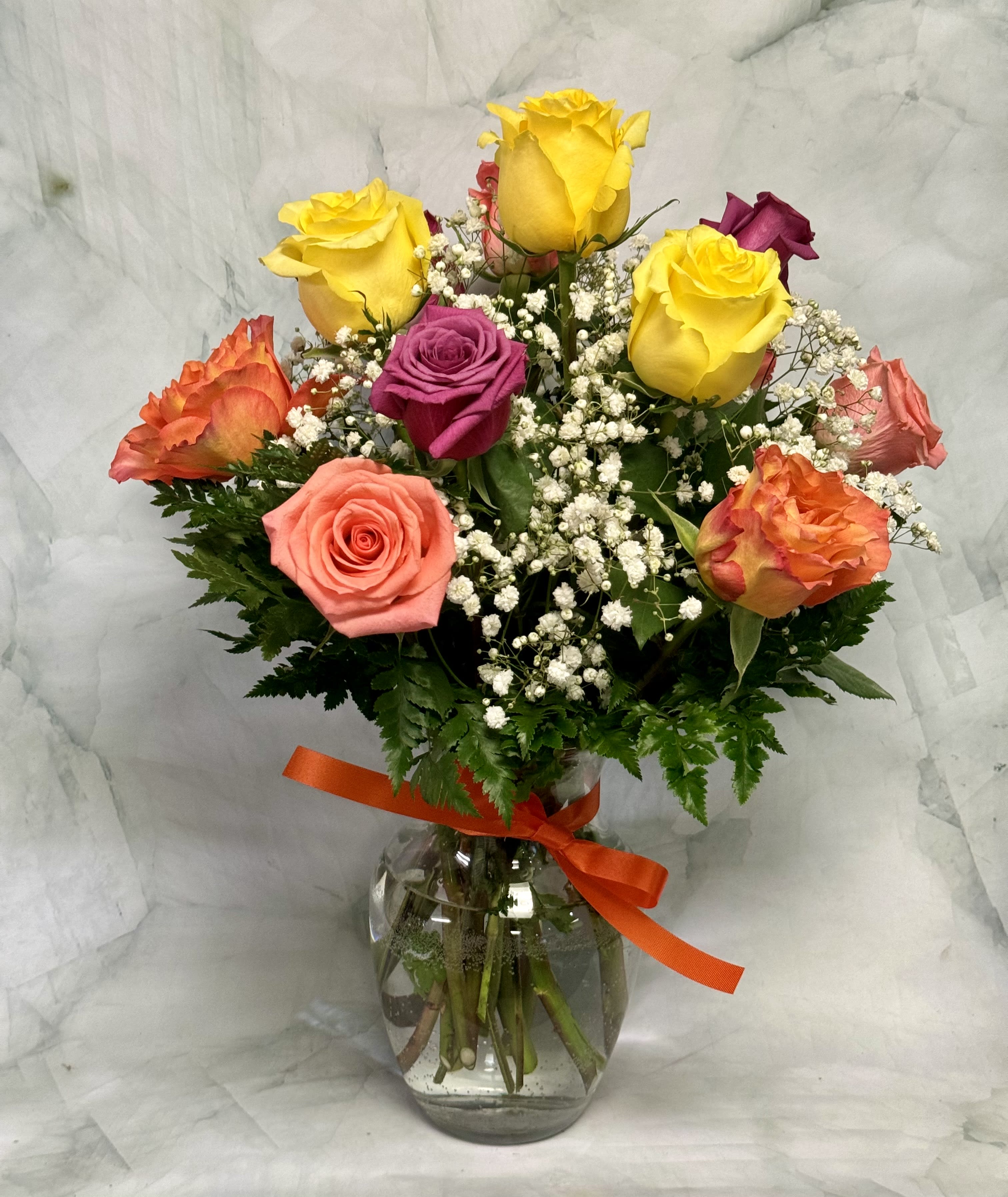 Dozen Mixed Pastel Roses Arranged in a Vase - A dozen beautiful assorted roses come arranged in a crystal clear glass vase. The arrangement includes greens, baby's breath, and of course a hand tied ribbon to match. Our roses come in a variety of colors. Let our designers mix you up a pretty dozen. If there is a color you prefer, feel free to let us know. Our job is to make them smile. 