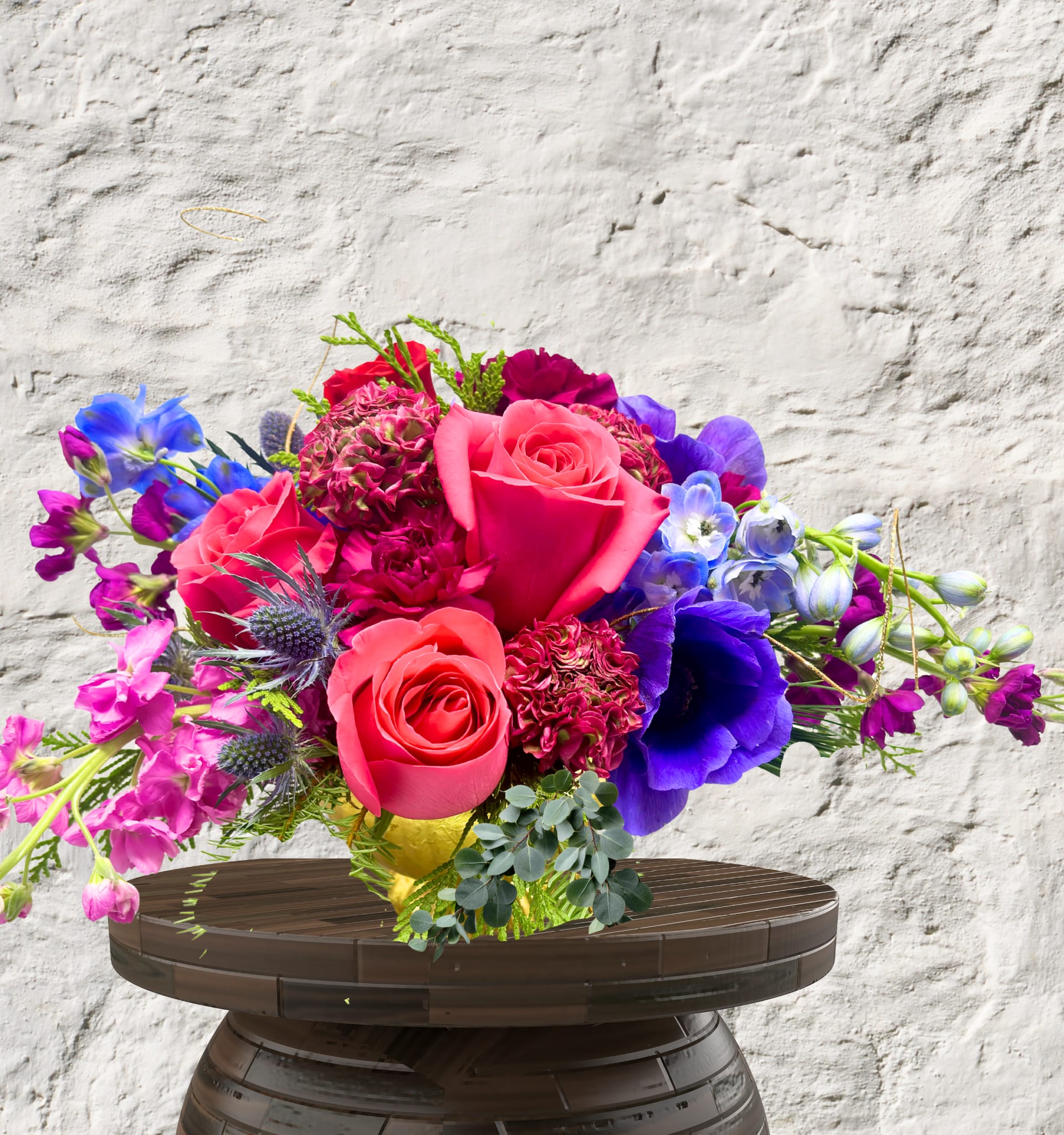 Velvet Romance Centerpiece - Bold Artistry. Golden Elegance. Unforgettable Luxury.  The Velvet Romance is a masterclass in texture and tonal depth. This arrangement is designed for the bold at heart, blending deep, passionate crimsons with moody purples and delicate, ethereal accents. Every stem is chosen for its "wow" factor, creating a lush, rounded silhouette that commands attention from every angle.  The Design &amp; Florals This arrangement showcases our "Vibrant &amp; Bold" weekly palette at its most luxurious.  Premium Blooms: Featuring a dense core of velvet-petaled roses and ruffled carnations, accented by the whimsical movement of sweet peas and the structural elegance of delphinium.  Textural Accents: We’ve layered in seasonal greenery, delicate gold-toned fillers, and organic elements like miniature cones to provide a multi-dimensional, garden-to-table feel.  The Upscale Vessel: Presented in a stunning, footed golden compote with a ribbed, metallic finish. This heirloom-quality vessel adds a regal warmth to any setting and is designed to be a permanent treasure in your home.  Versatile Luxury While perfect as a statement piece for your dining table or entryway, the Velvet Romance is a favorite for high-end wedding centerpieces. Its sophisticated scale and rich color story provide a lavish focal point that feels both classic and contemporary.