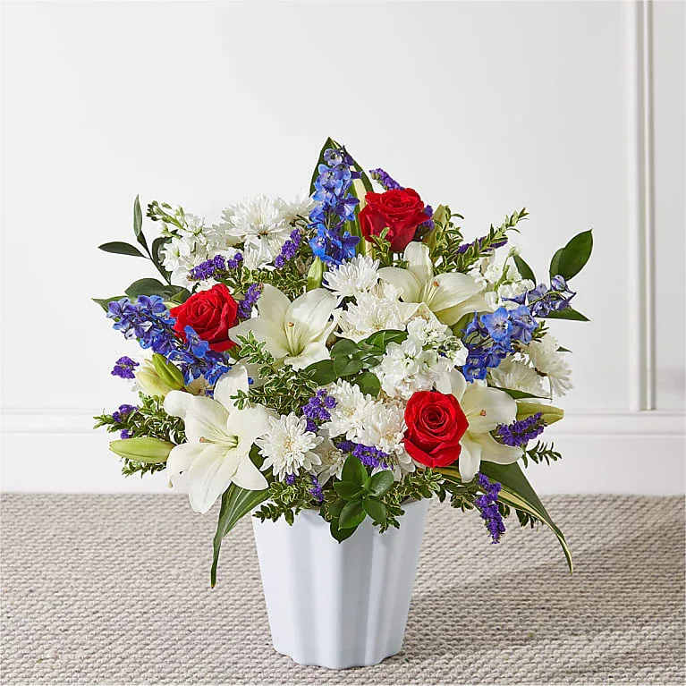 Consoled Floor Basket - A collection of red roses, blooming white lilies, and blue delphinium come beautifully arranged to beautifully accent a service.