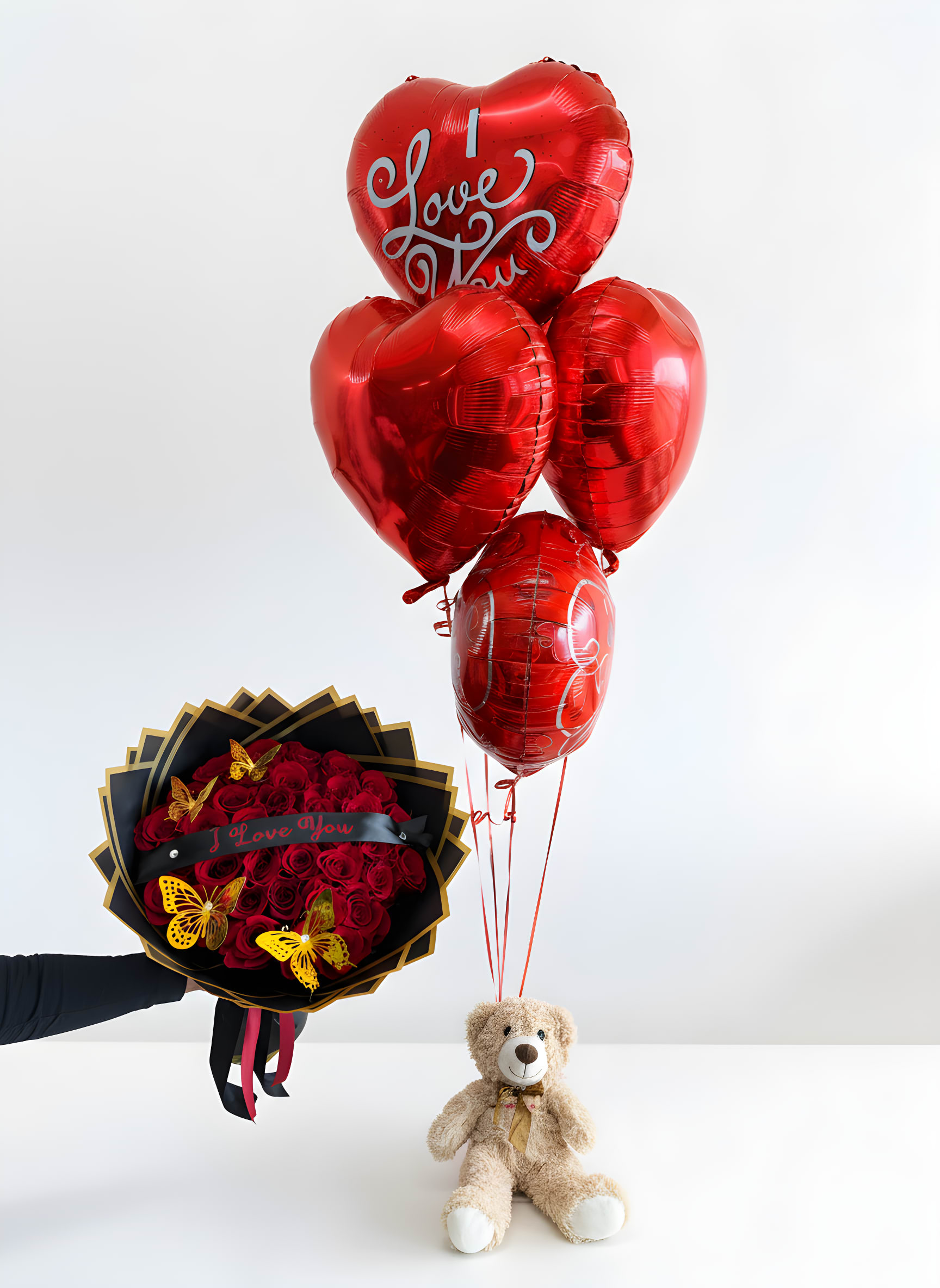 Say I Love You Bundle - Make a bold romantic statement with our Say I Love You Bundle. This unforgettable gift includes a stunning wrapped bouquet of fresh red roses adorned with delicate butterflies, a charming “I Love You” banner, an adorable teddy bear, and a bundle of 5 red heart-shaped helium balloons. Perfect for anniversaries, Valentine’s Day, proposals, or simply to remind someone how deeply they are loved—this bundle delivers romance from every angle. STANDARD 24 ROSES DELUXE 36 ROSES PREMIUM 50 ROSES