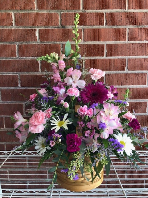 BASKET OF DELIGHT - An arrangement of pink roses, purple and pink daisies, larkspur, alstroemeria  and wax flower in a wicker basket that is sure to bring delight.