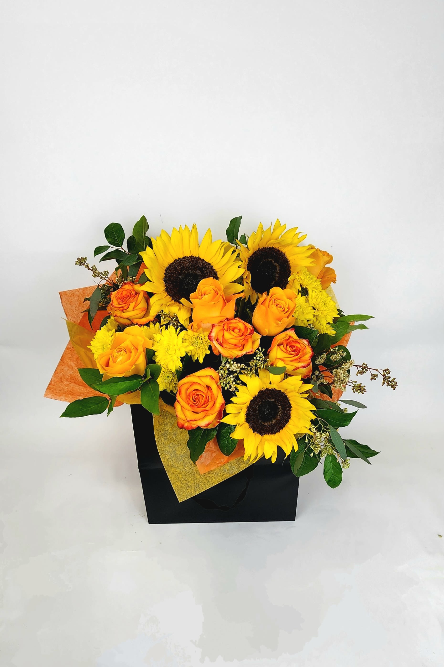 Sunset vibes - A bouquet of bright, warm colors, including sunflowers, roses, and fillers wrapped in tissue paper and inside of a paper box .