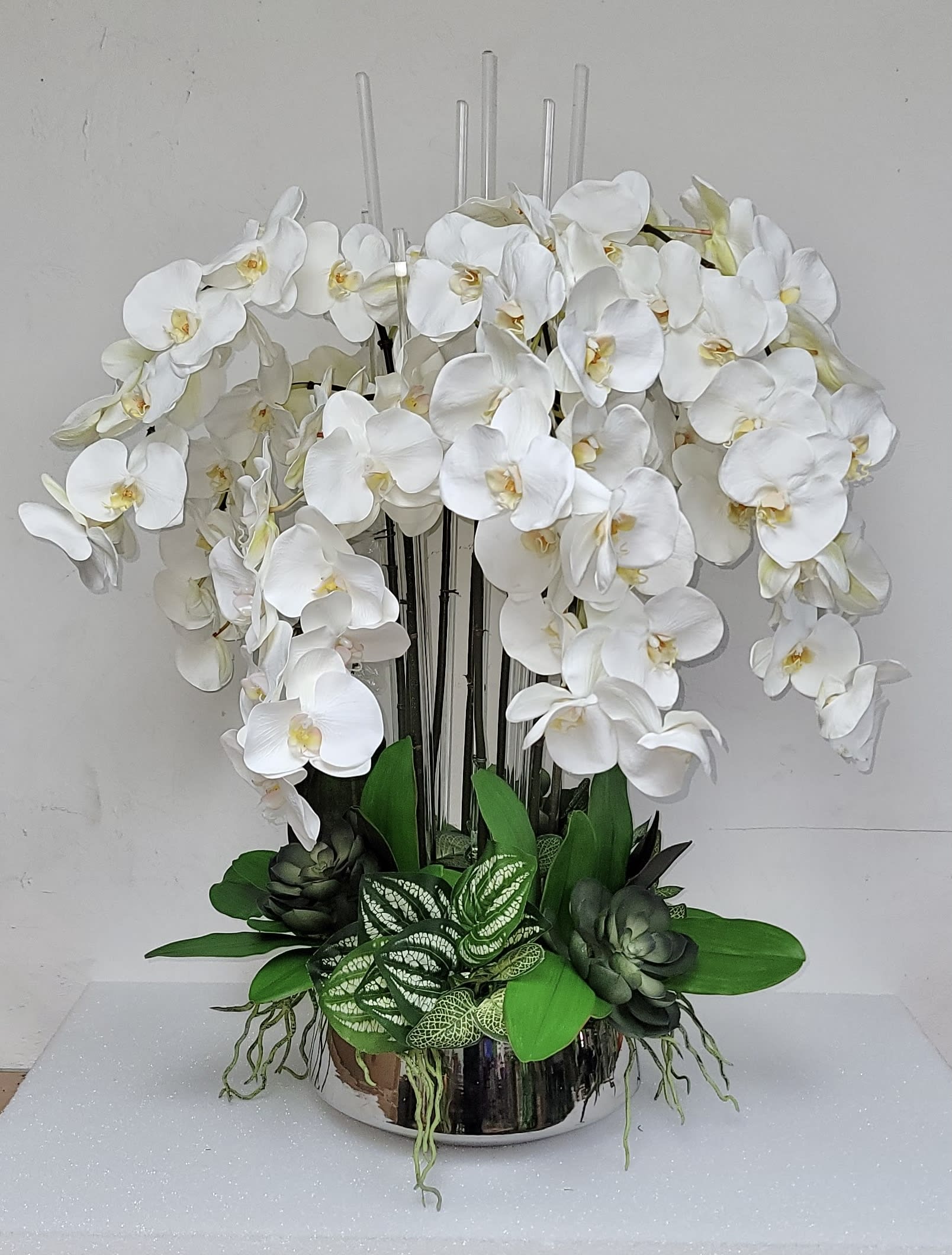 White Orchid Jungle  - Silver low cylinder whit 8 orchid stems &amp; greens.  (If a silver base is not available, a white vase would be used) There is a window off 24 business hours to fulfill these order 