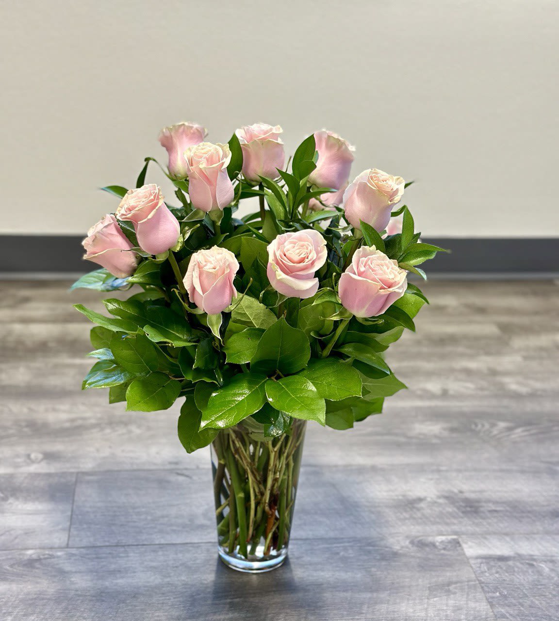 1 Dozen Light Pink Roses - A joyful gesture of love and affection, this chic arrangement of light pink roses with fresh greens is a special surprise on any occasion. The light pink roses are arranged with salal and delivered in a clear vase.