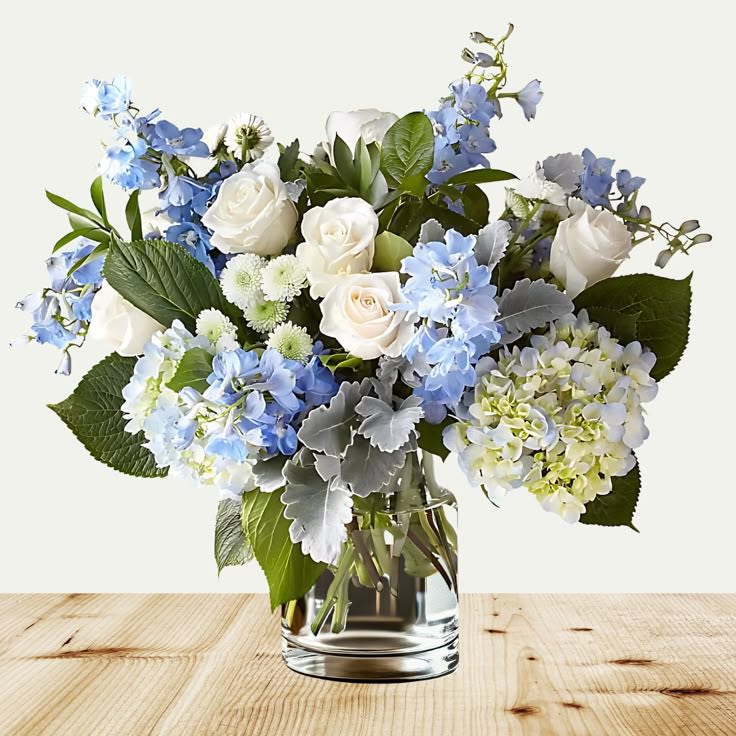 Clear Skies Bouquet - Bring a breath of fresh air into any space with our Clear Skies Bouquet – a serene blend of elegance and tranquility. This stunning arrangement features soft white roses, sky-blue delphiniums, delicate hydrangeas, and textured accents of dusty miller and lush greenery, all artfully arranged in a sleek glass vase. Perfect for birthdays, anniversaries, sympathy gestures, or simply brightening someone’s day, this bouquet captures the peaceful beauty of a clear, cloudless sky. Its gentle color palette of whites, blues, and greens evokes calm and comfort, making it a timeless gift for any occasion. Features: Hand-arranged with premium blooms Delivered in a classic clear glass vase Ideal for home décor or thoughtful gifting Let the Clear Skies Bouquet send your sentiments with grace and beauty.