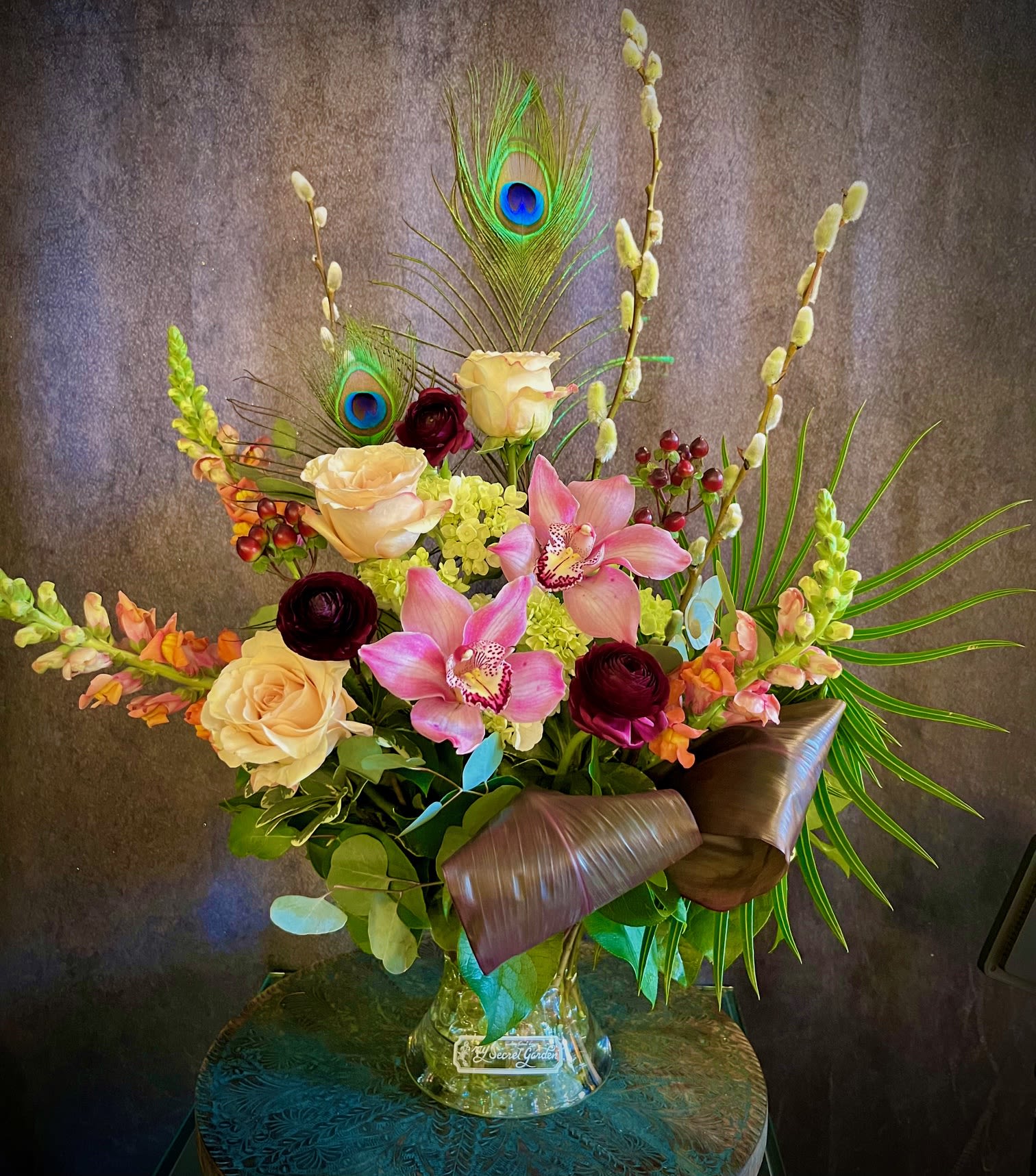 Art Nouveau - This beautiful arrangement reminiscent of the the Art Nouveau period features beautiful Roses, deep purple Ranunculus, Hydrangea, Snap Dragons, Cymbidium Orchids and keepsake Peacock feathers. With a wonderful mix of light and dark colors, "Art Nouveau" is the perfect classy arrangement for any occasion. 