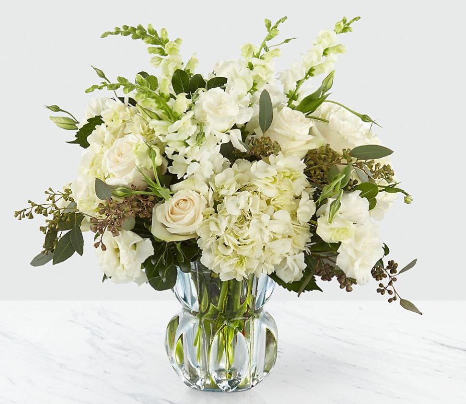 Gala™ Luxury Bouquet - There's something about simplicity that just gives off the sense elegance. Comprised of classic white blooms and luscious greens set in a subtle blue heavyweight glass vase, the pure beauty of the bouquet instantly draws you in. Vendela roses, snapdragons, and hydrangea capture a truly refined bouquet. 