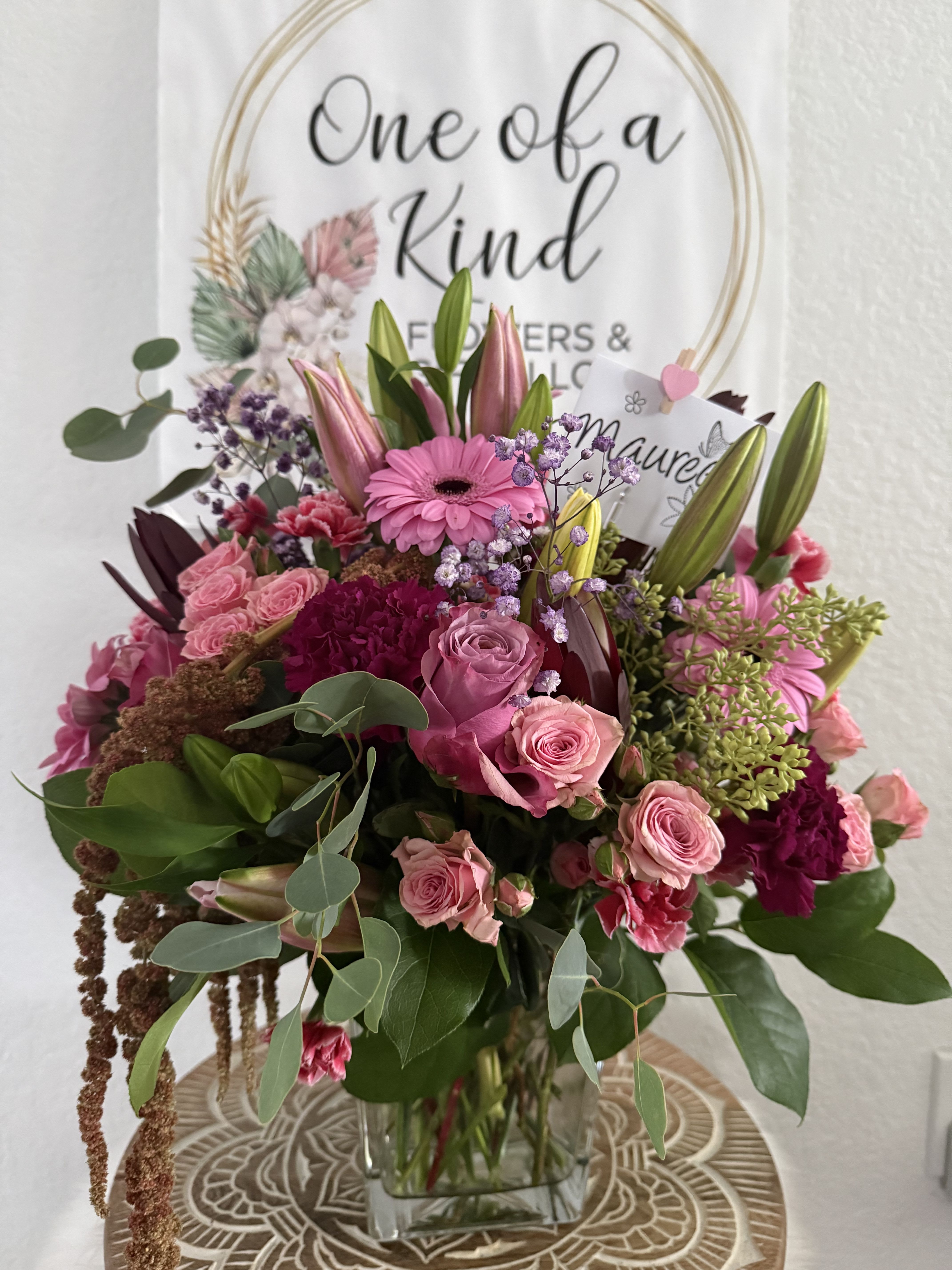  Rosy Dreams Arrangement - An elegant and vibrant floral arrangement filled with rich textures and stunning color. Designed in a clear glass vase, it features soft pink roses, lilies, gerberas, carnations, and delicate wildflower accents that bring freshness and movement. Shades of pink, fuchsia, and green blend beautifully to create a harmonious composition—perfect for birthdays, anniversaries, thank-you gifts, or brightening any space. A sophisticated and meaningful gift crafted to create unforgettable moments.