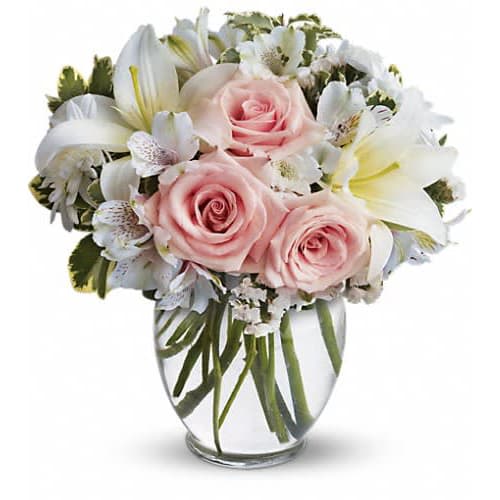Compact bouquet of pale pink roses and white lilies in a clear glass vase