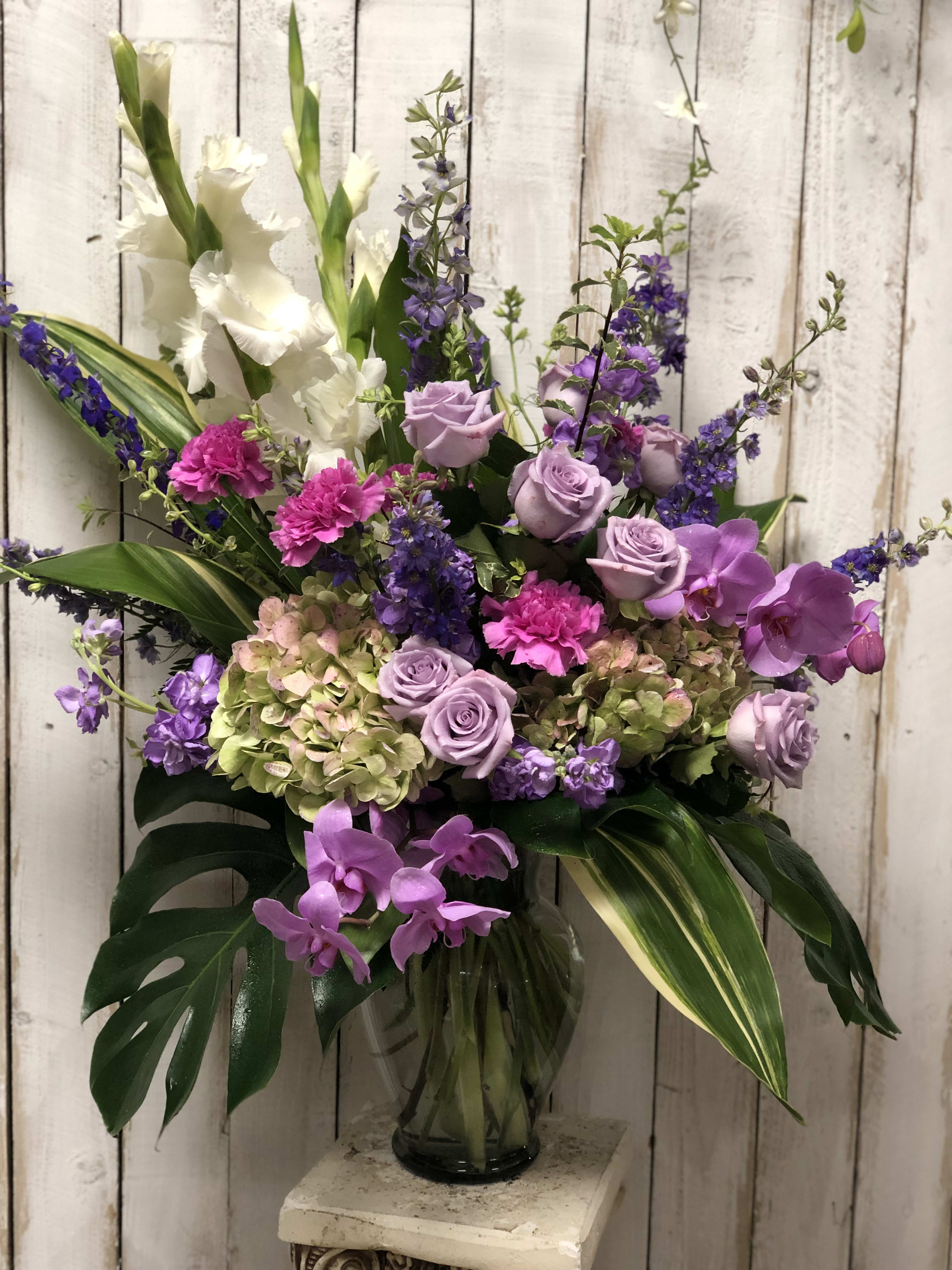 Lavender Meadows - This stunning design is arranged in a glass vase containing orchids, larkspur, roses, carnations, gladiolus and hydrangeas.