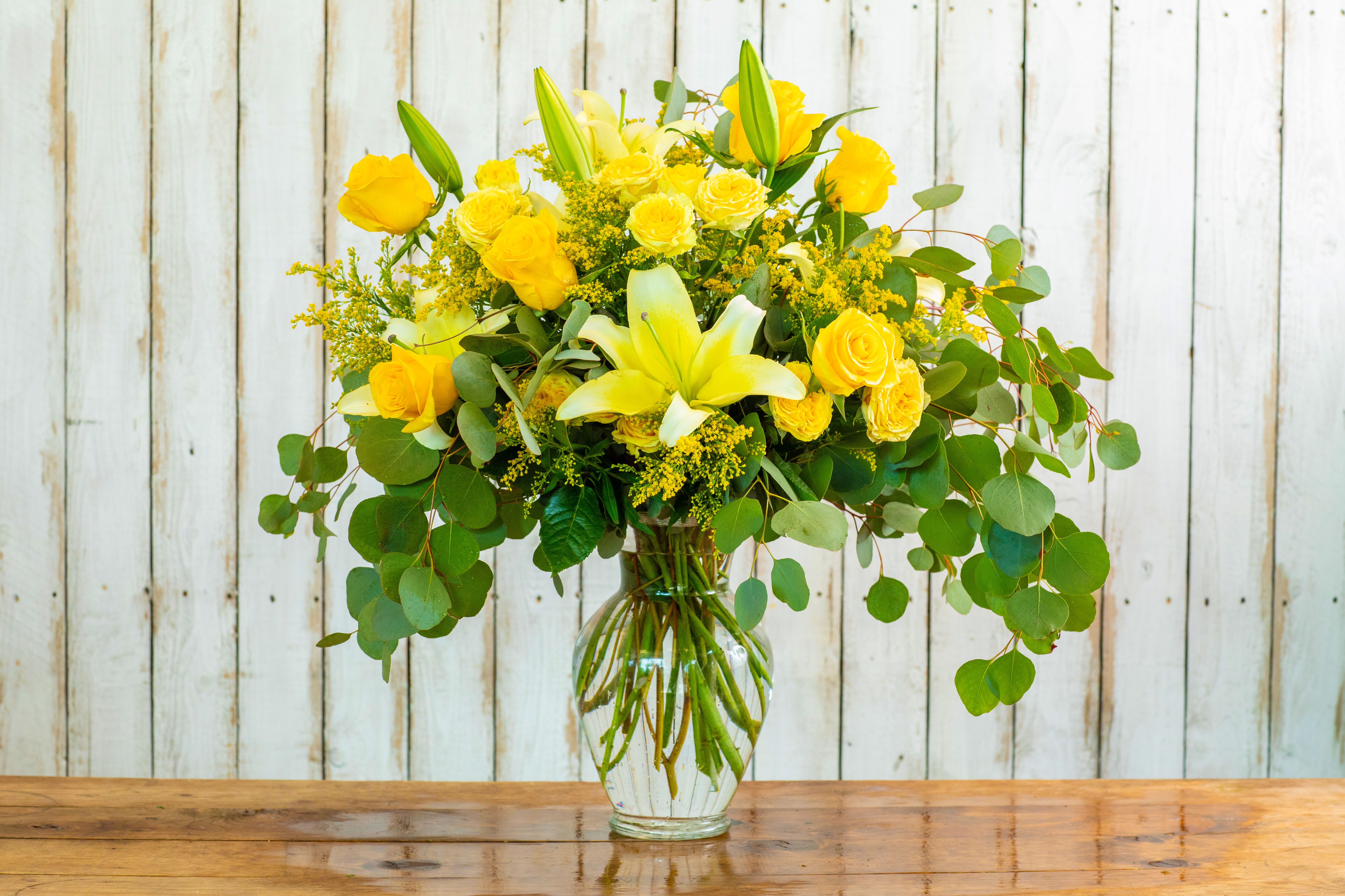Golden Sunshine Bouquet - Brighten any space with the Golden Sunshine Bouquet, a spectacular and vibrant arrangement meticulously crafted by your premier Rancho Cucamonga Florist. This abundant bouquet radiates warmth and joy with its luxurious display of cheerful yellow blooms.  It features elegant yellow lilies, surrounded by classic yellow roses and delicate spray roses, all accented with golden solidago (filler flowers) and lush, rounded eucalyptus leaves. This grand arrangement is beautifully presented in a classic clear glass vase, making it an impressive gift to send for any occasion.  As the leading Rancho Cucamonga flower shop, we make it simple to shop online for flowers. This radiant arrangement is the perfect choice for a celebratory birthday bouquet, a thoughtful get well soon surprise, a magnificent anniversary gift, or simply to bring a burst of happiness to someone's day.  We offer reliable same-day flower delivery throughout the entire Rancho Cucamonga area. Don't miss out—order flowers now and trust our expertise to deliver a stunning and unforgettable arrangement. Buy flowers online today with confidence from your dependable local Rancho Cucamonga Florist!
