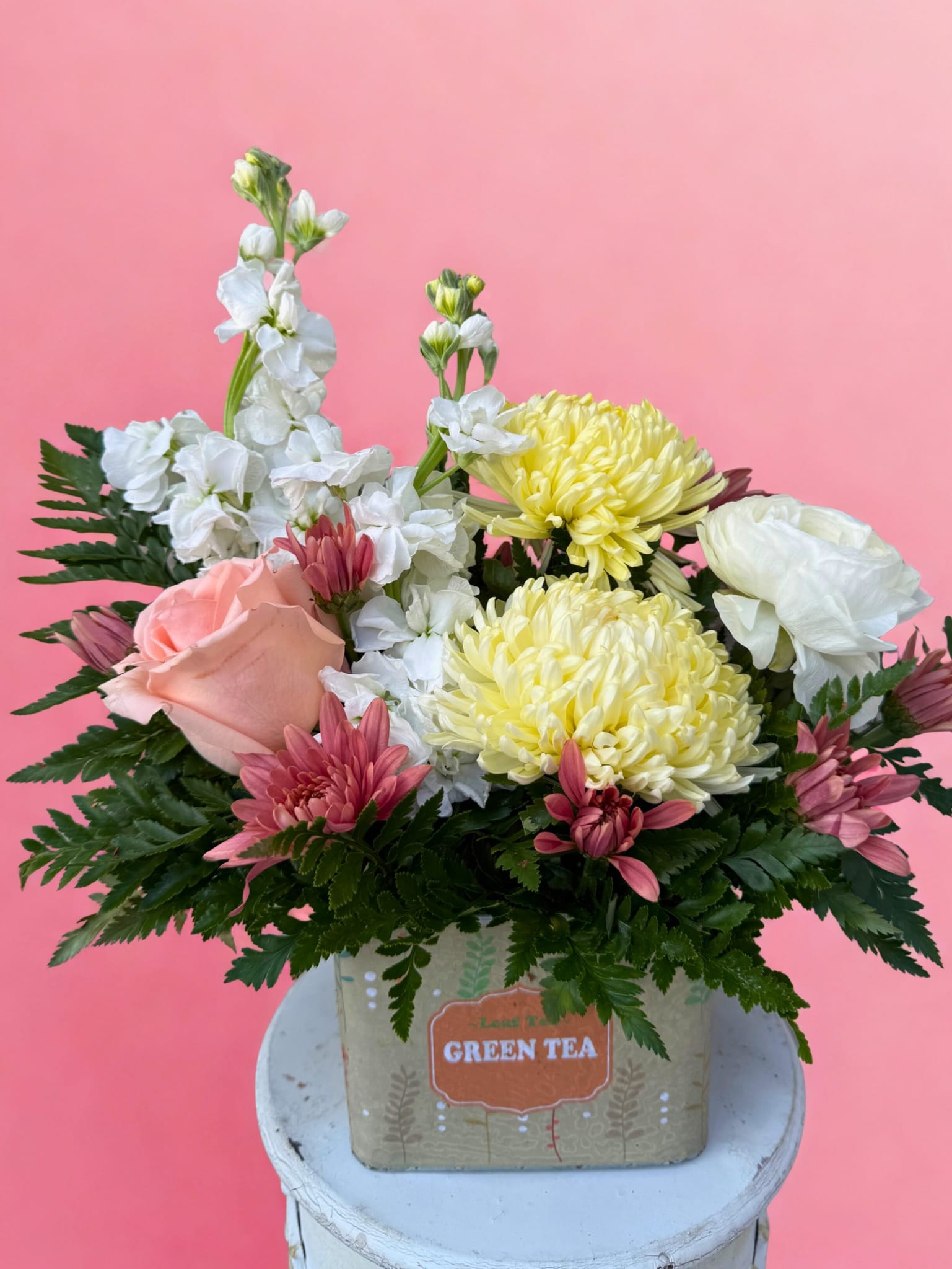 Tea Time Blooms - Fresh, cheerful, and effortlessly charming — Tea Time Blooms brings a little sunshine to every day. Arranged in a sweet tea-themed container in soft green, yellow, and cream hues, this design feels like a warm afternoon pick-me-up. Bright yellow cremones add happy pops of color, while romantic white ranunculus and fragrant white stock create an airy, elegant base. Peach roses and salmon cushions finish the look with gentle warmth and softness. Perfect for thank-yous, birthdays, or just because — this arrangement is a delightful way to steep someone’s day in beauty.   All flowers, floral colors, and containers are subject to change due to availability.
