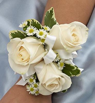 White Corsage - Elegant white roses, white Monte casino and variegated pittosporum laced with white ribbon creates an elegant accompaniment for the mother of the bride or groom, grandmothers, or treasured relatives.  Hand-gathered corsage arrangement of graceful white roses and white Monte casino, accented with variegated pittosporum 