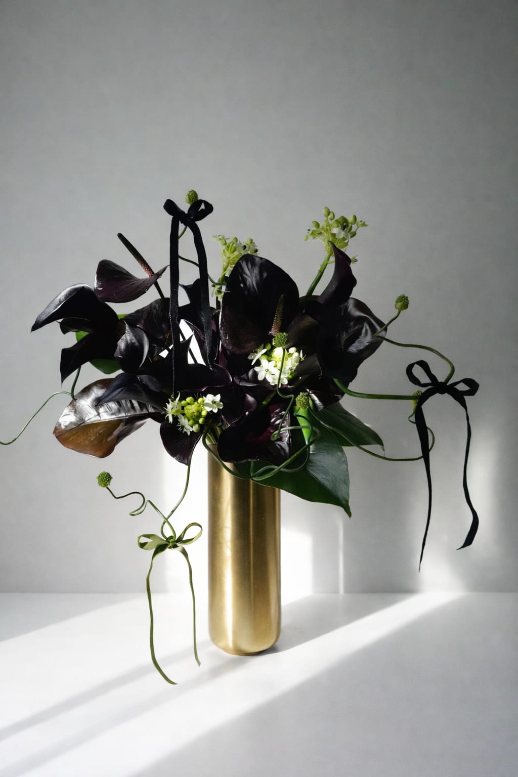 Gilded Eclipse  - Gilded Eclipse is a dramatic floral composition where shadow meets gold.  Deep-toned anthuriums and sculptural botanicals rise from a gilded vessel, creating contrast between darkness and luminosity.  Intentional lines, restrained movement, and rich texture transform this arrangement into a bold, modern statement piece.    