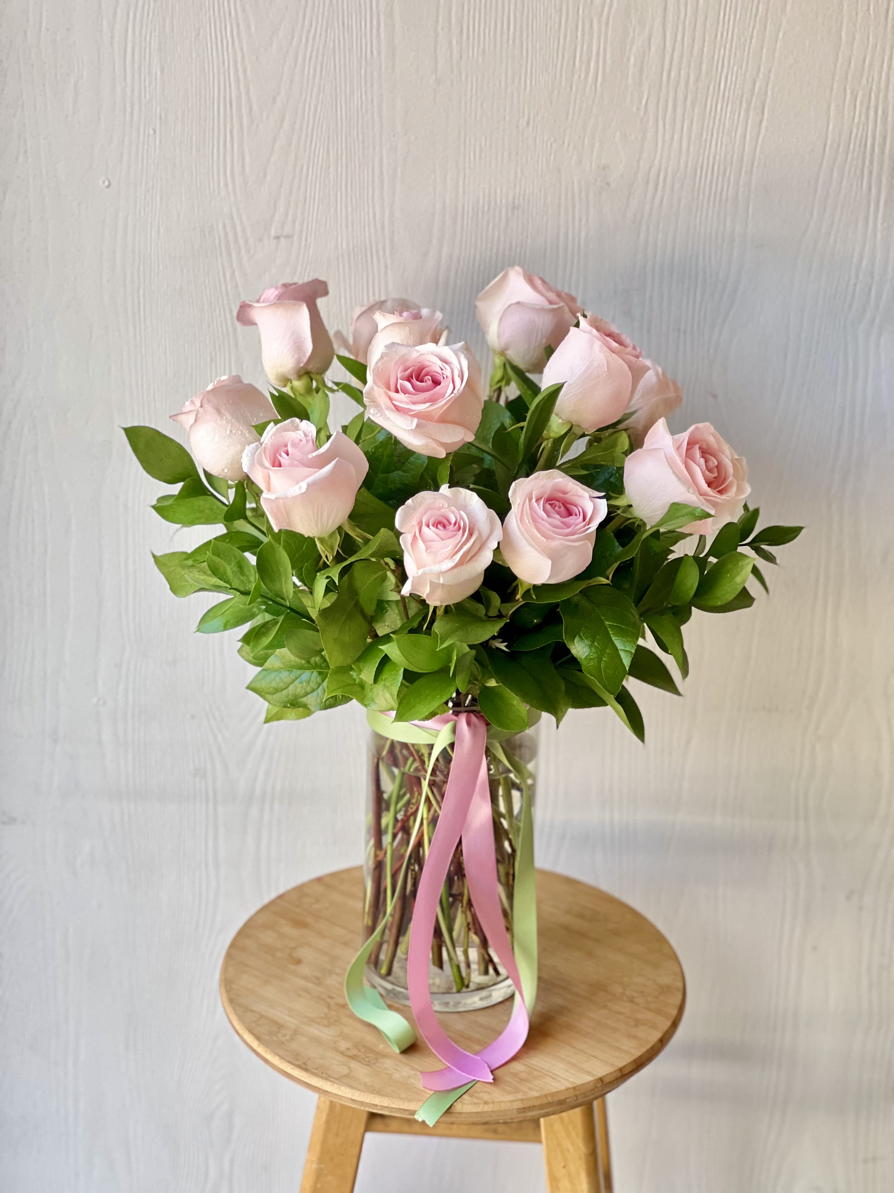 EC116  Classic Long Stem Pink Roses - Celebrate any occasion with the timeless elegance of our 1 Dozen Pink Rose Bouquet. This stunning arrangement features twelve hand-selected, premium pink roses, carefully arranged in a clear glass container. Each rose is a symbol of grace, admiration, and love, making this bouquet the perfect gift for someone special or a beautiful addition to your own home.  The roses are wrapped with a soft satin ribbon that adds a touch of charm, elevating the presentation to a new level of sophistication. The glass container showcases the beauty of the roses while providing a classic, clean look that complements any décor.  Whether it’s a birthday, anniversary, or just because, this pink rose bouquet is sure to leave a lasting impression.  The deluxe bouquet features 2 dozen roses.