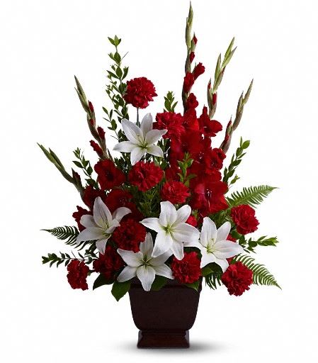 T227-1A Teleflora's Tender Tribute - Vivid and touching, vibrant reds and serene whites blend in honor and celebration of a life filled with love, light and grace. Beautiful fresh flowers such as red gladioli and carnations with white asiatic lilies set amidst myrtle, sword fern, and salal in an exclusive Noble Heritage Urn.  
