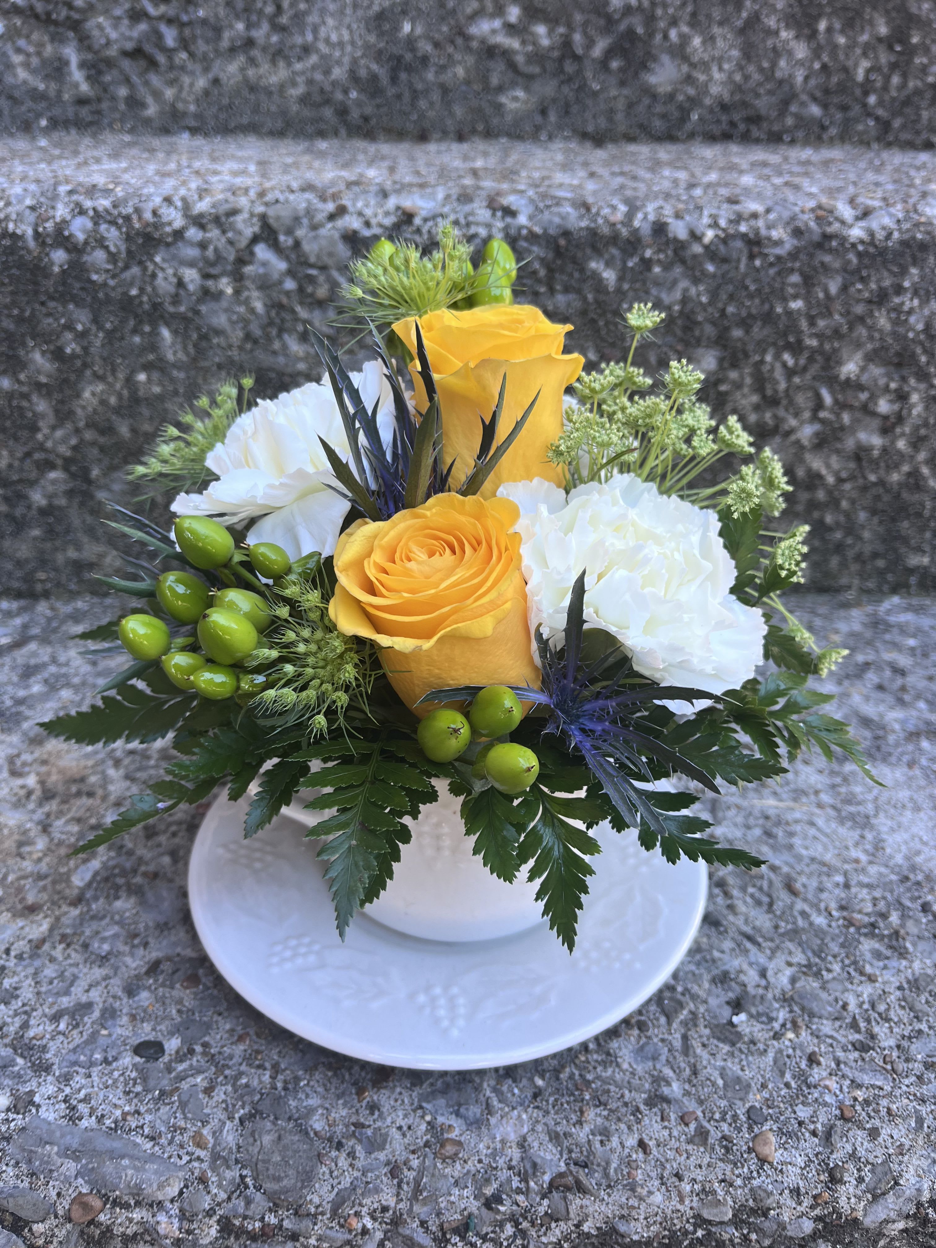 Sip of Sunshine Coffee Cup - This cute arrangement has queen Ann’s lace, yellow roses, thistle, hypericum and green carnations with greenery. 
