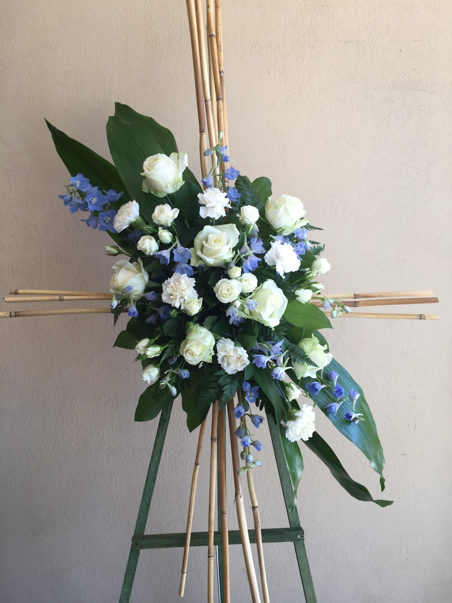 CROSS IN TO HEAVEN - BAMBOO CROSS  TO GUIDE YOUR LOVE ONE TO HEAVEN. WITH WHITE ROSES, BLUE DELPHINIUM, WHITE SPRAY ROSES AND WHITE CARNATIONS