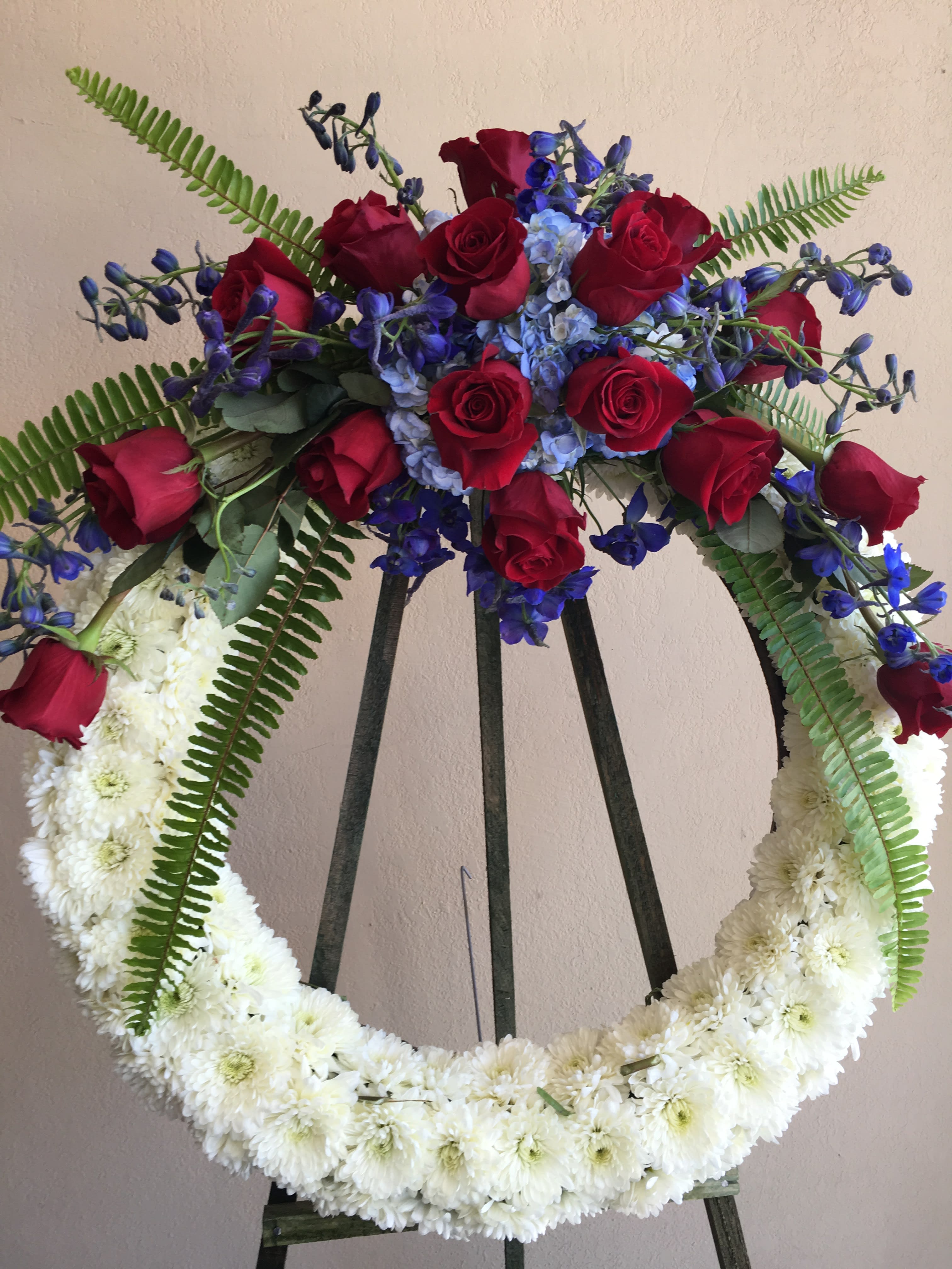 NEVER FORGET ME - CIRCULAR WREATH WITH MUMS, HYDRANGEA, BLUE DELPHINIUM, AND RED ROSES  THE PERFECT FAREWELL 