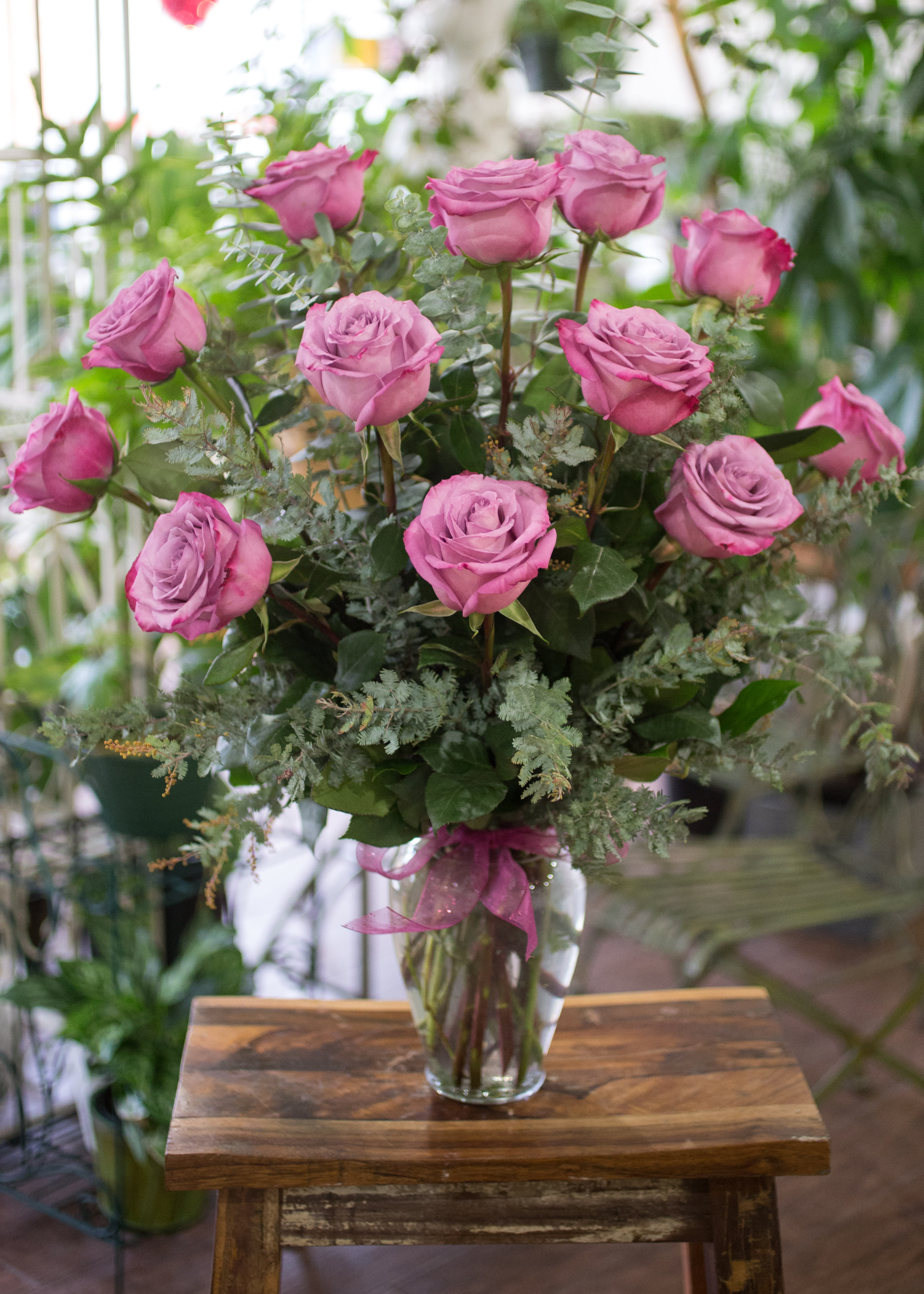 Babette - One dozen highly fragrant, purple Moody Blues Roses, beautifully arranged in a clear glass vase with seasonal accents and foliage.