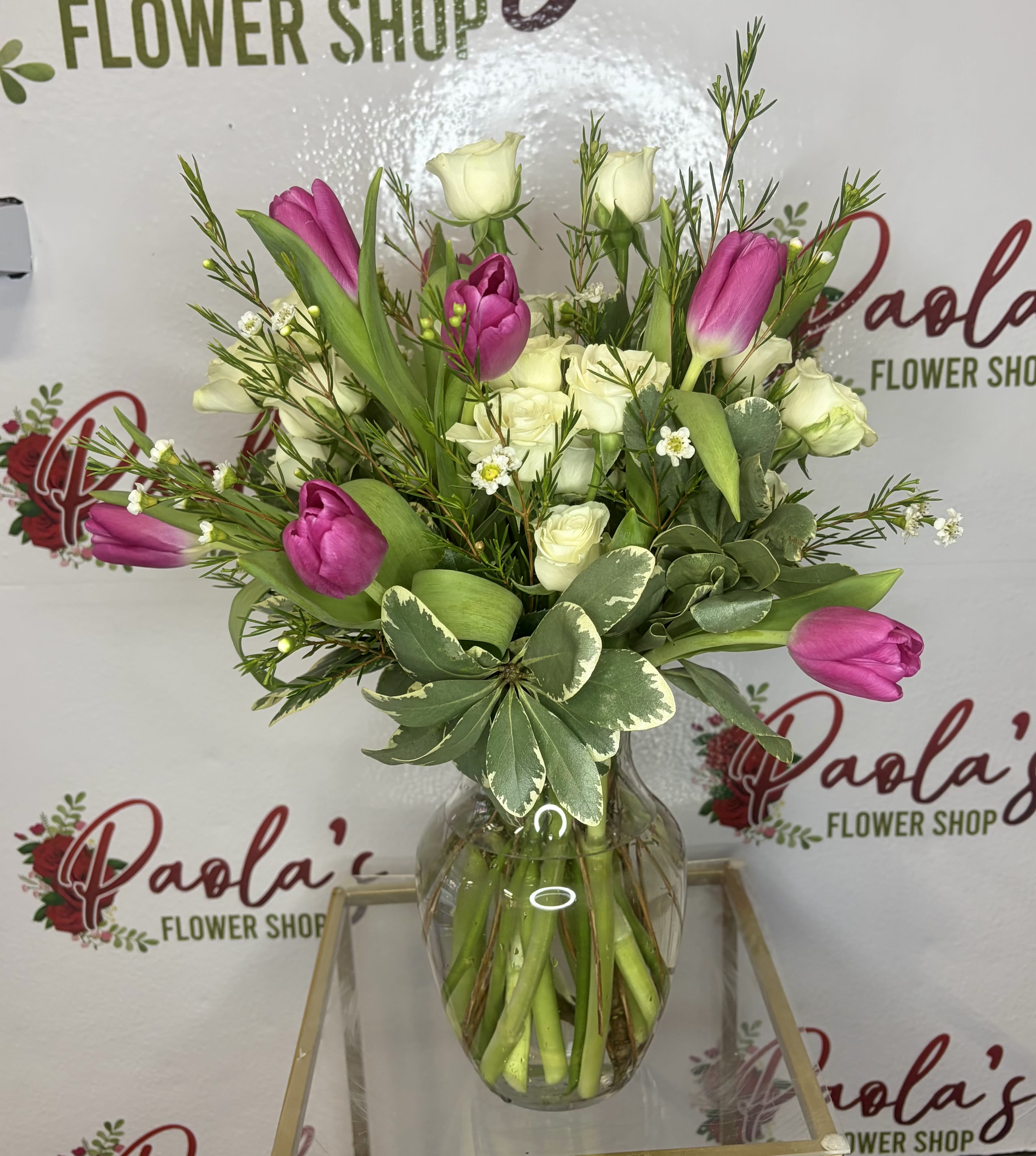 Spring Elegance - A graceful vase arrangement featuring fresh pinky tulips*, creamy white spray roses, and delicate accent blooms surrounded by lush greenery. Designed in a clear glass vase, this arrangement brings a soft, natural charm that brightens homes, offices, or heartfelt celebrations. Perfect for birthdays, thank-you gifts, or simply making someone smile.   Tulips and spray rose color may change based on availability, this item will only be available through end of May 