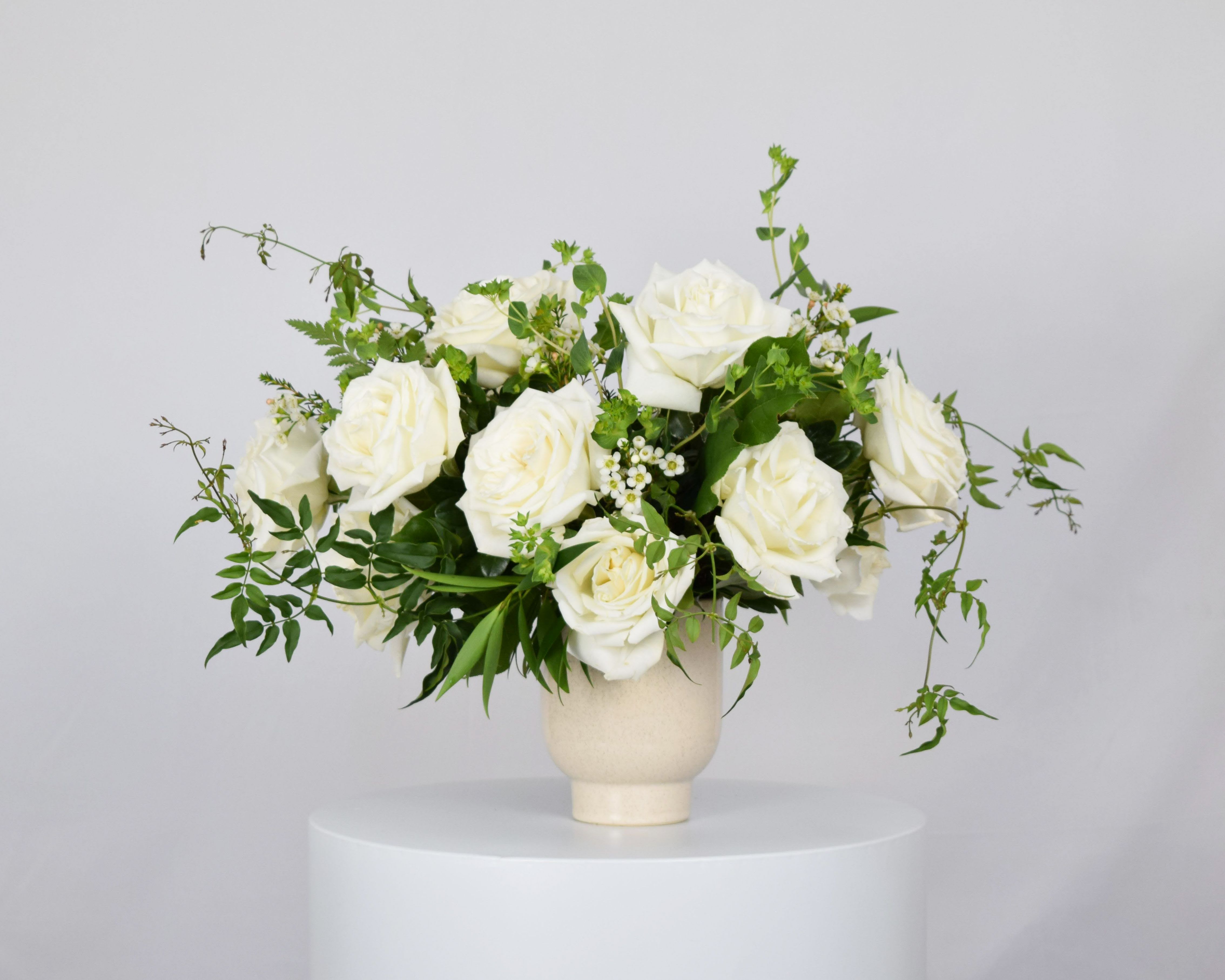 Garden-Style One Dozen Roses - This romantic garden-style arrangement features one dozen roses paired with fragrant jasmine vine and a variety of flowy, textured greenery. Designed in a medium compote, it can be customized with your choice of rose color— Pink Expression, Quicksand, Red Hearts, Playa Blanca, Veggie, Black Baccara, Shimmer, Buttercup, or Free Spirit. Please specify your preferred rose color in the order notes for a personalized, naturally elegant bouquet.  Please note: Due to seasonal availability, some blooms may be substituted—but always with equally lush, premium stems to maintain the overall look and feel of the design.