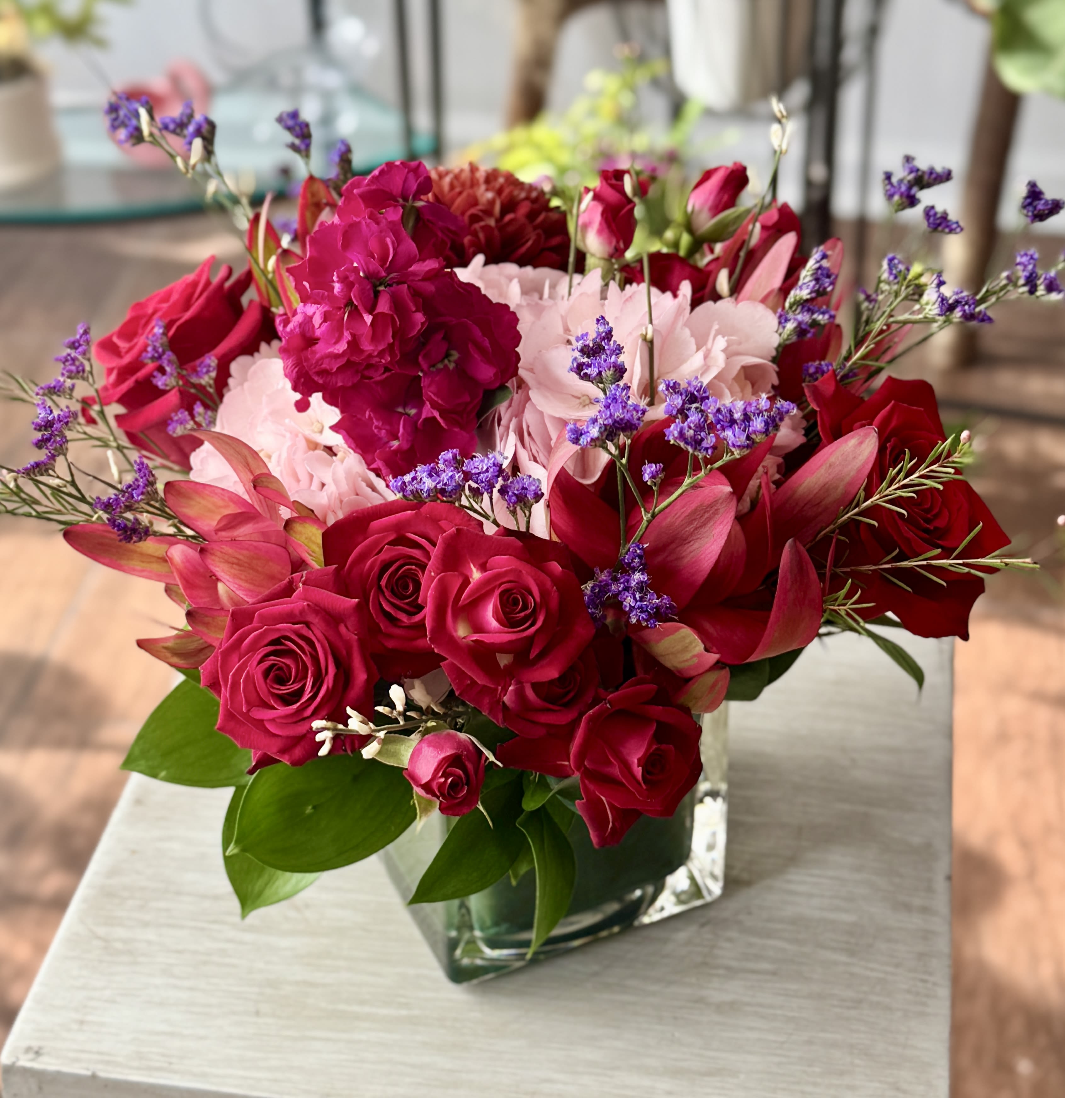 Victoria - Red and pink flowers arranged in a clear glass cube vase. 