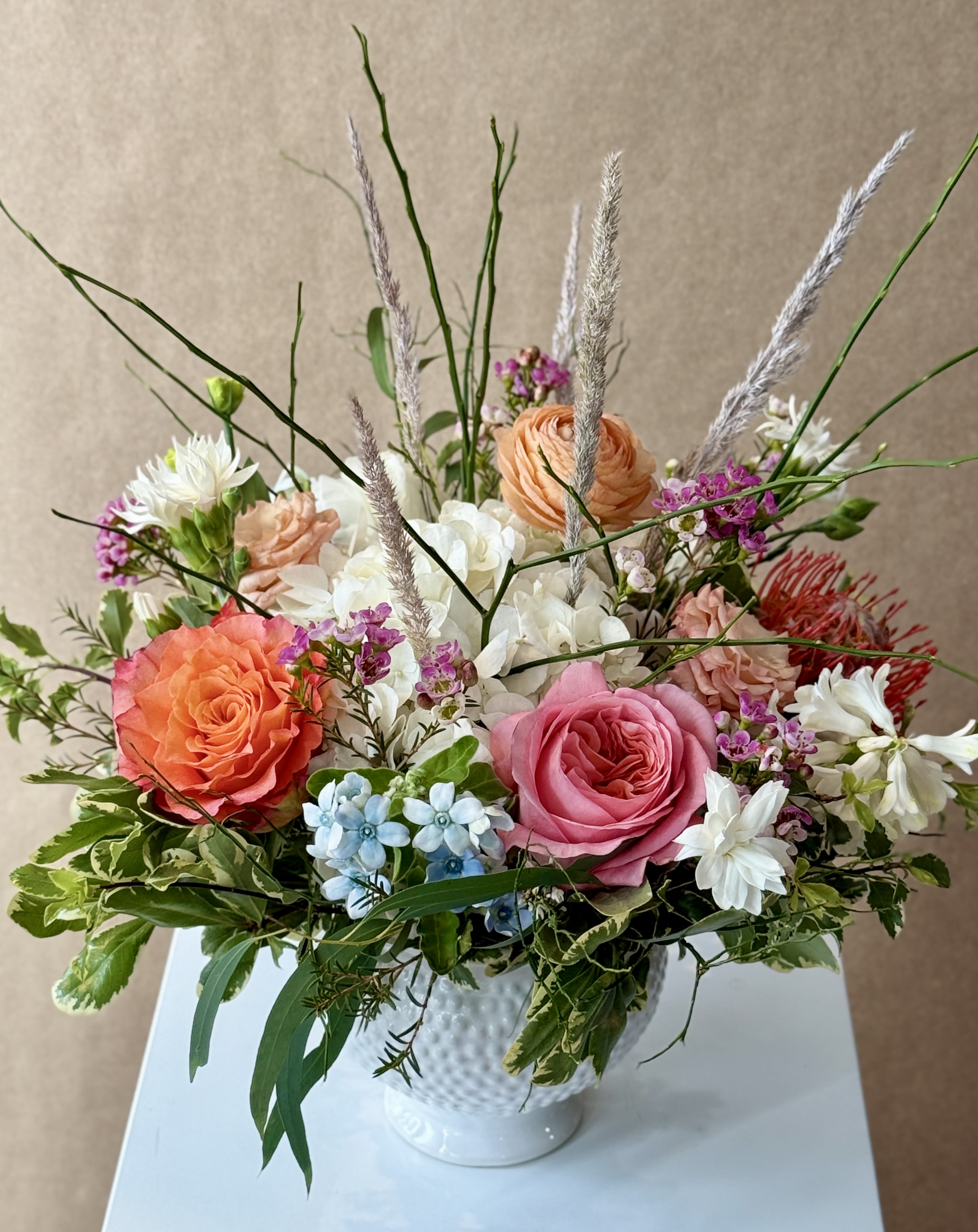 Alessandra - Variety of blooms and interesting textures in a white ceramic vase.