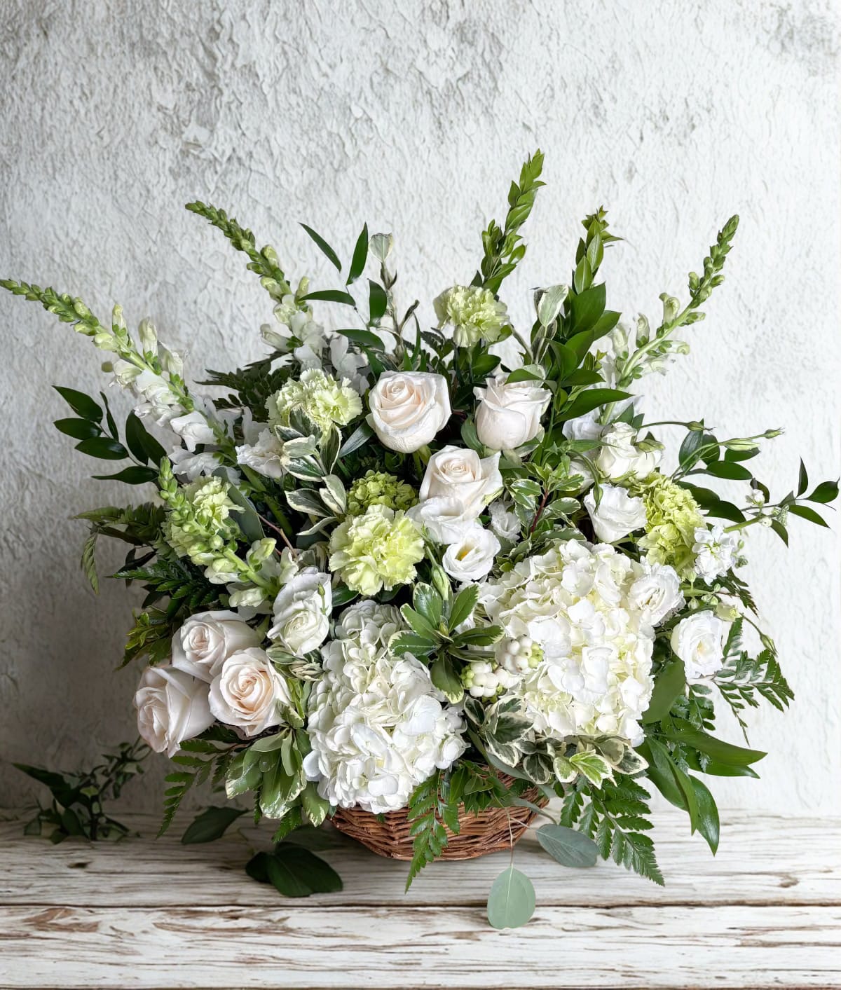 Sympathy Traditions  - Send your heartfelt sympathy - This traditional design is created in a natural wicker basket and is one of our most popular choices for flowers to send to the services.  We most often recommend a palette of whites, creams and greens, however we are happy to design a seasonal color palette as well.   Please call the shop for any specific needs.  Ribbon shown here as example.  Size shown is the deluxe, Approx. 15"x30"  **** We do not recommend this as a gift to a residence ****