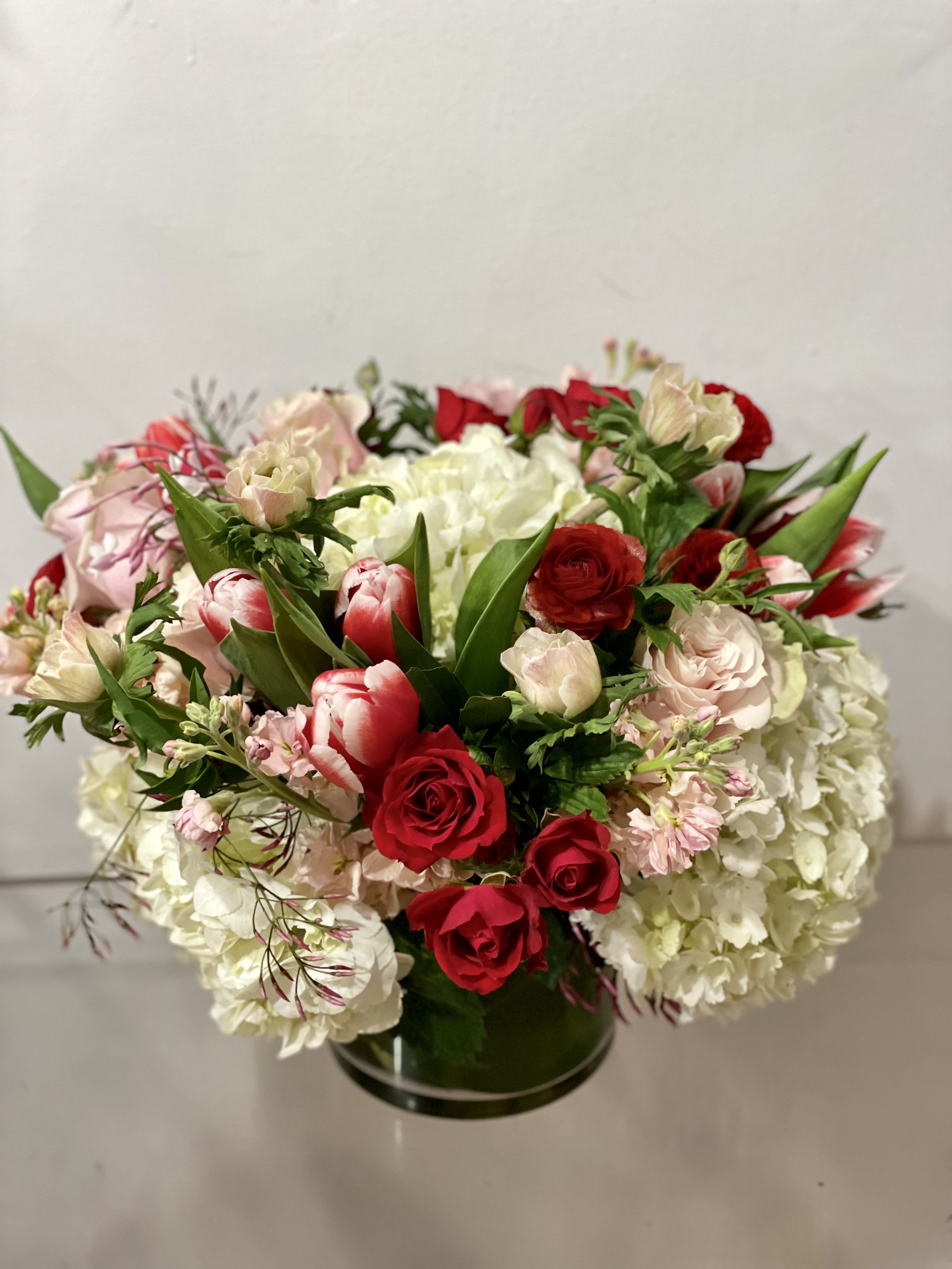Hello love - This arrangement is a designers choice in pink, white, and red with premium blooms in a ti leaf lined vase. You choose the size, we choose the blooms!   NOTES: We will choose the freshest and most interesting ingredients at the market to make this arrangement shine. Vessels may be substituted depending on availability.    