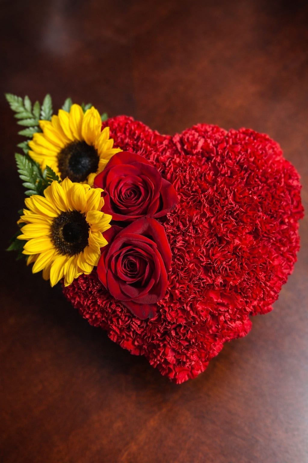 Sunset love heart  - Sunset Love Heart A romantic heart-shaped arrangement featuring red carnations, red roses, and bright sunflowers. Designed to express love and warmth, this elegant floral piece is perfect for anniversaries, Valentine’s Day, or any special