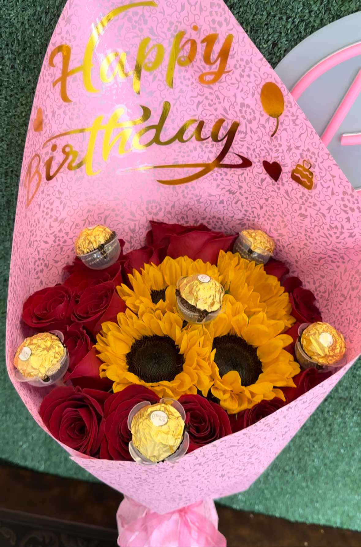 Happy birthday buchon - Hand bouquet with Roses, sunflowers and chocolates on a wrapping paper. Does not include vase "Picture is a reference every arrangement would not be exactly the same. Color Substitution may apply. Flowers and color substitution may apply"