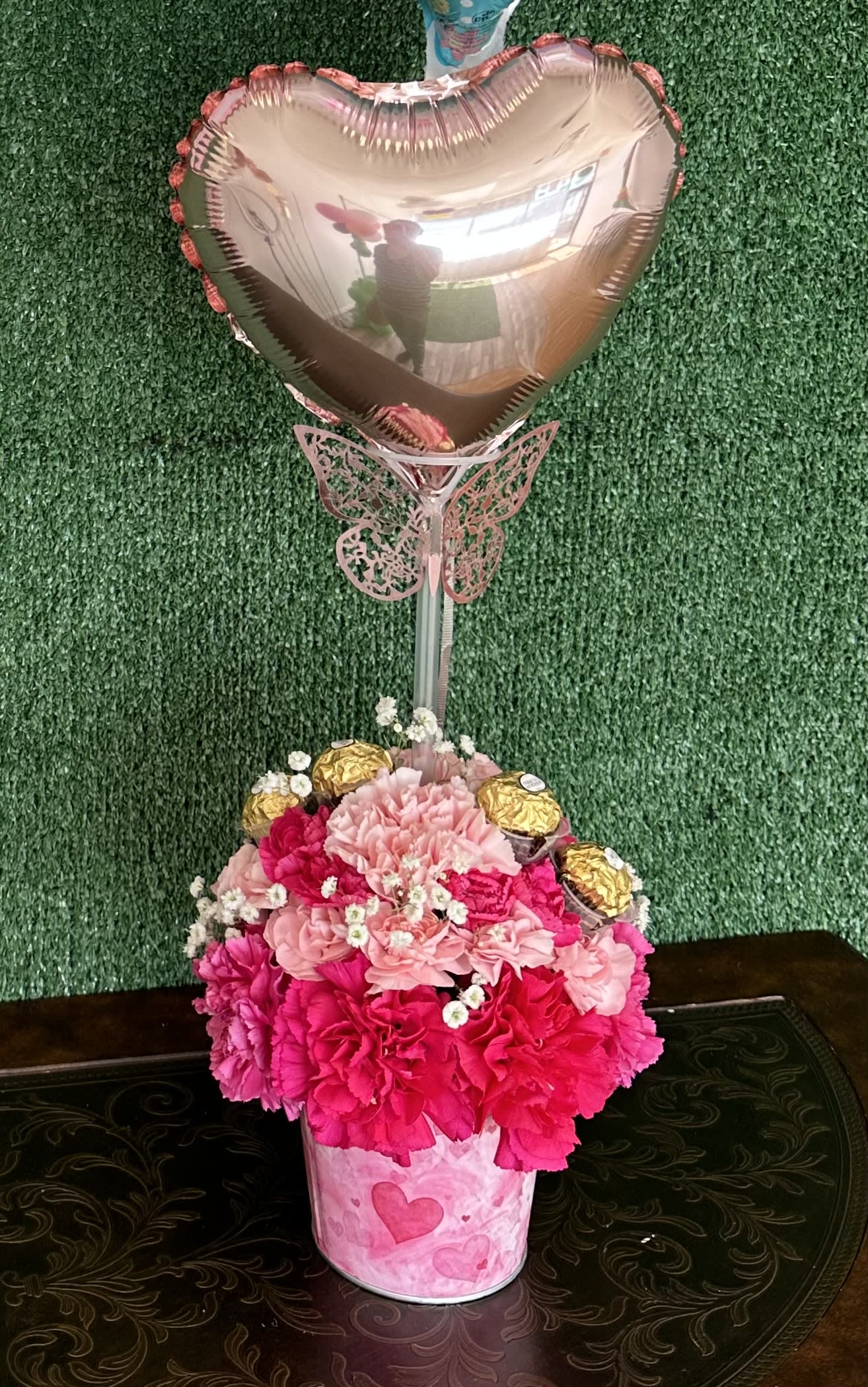 Pink Garden - Carnations and baby breath on a pink bucket with chocolates and custom balloon  "Picture is a reference every arrangement would not be exactly the same. Flowers and color substitution may apply"