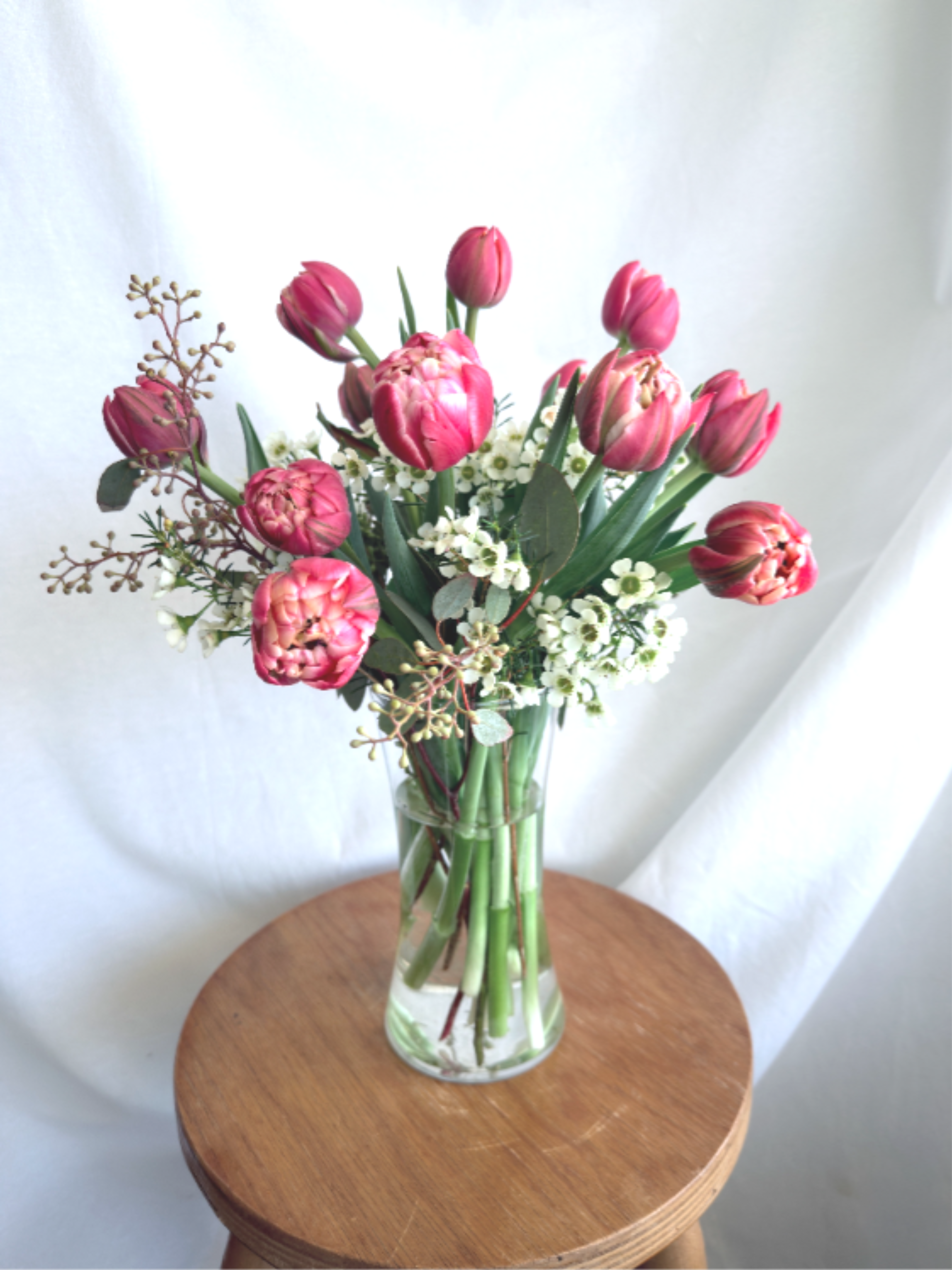 Sweet Tulips by the Dozen - Locally grown tulips are a treat for the season. Share a dozen (or two) in this simple vase arrangement. Accented with wax flower and seasonal greenery these long lasting beauties make a stunning gift for any reason. Tulips are available in your choice of red, pink, white or a mix of colors. Let us know your color choice in the notes section of the order form. 