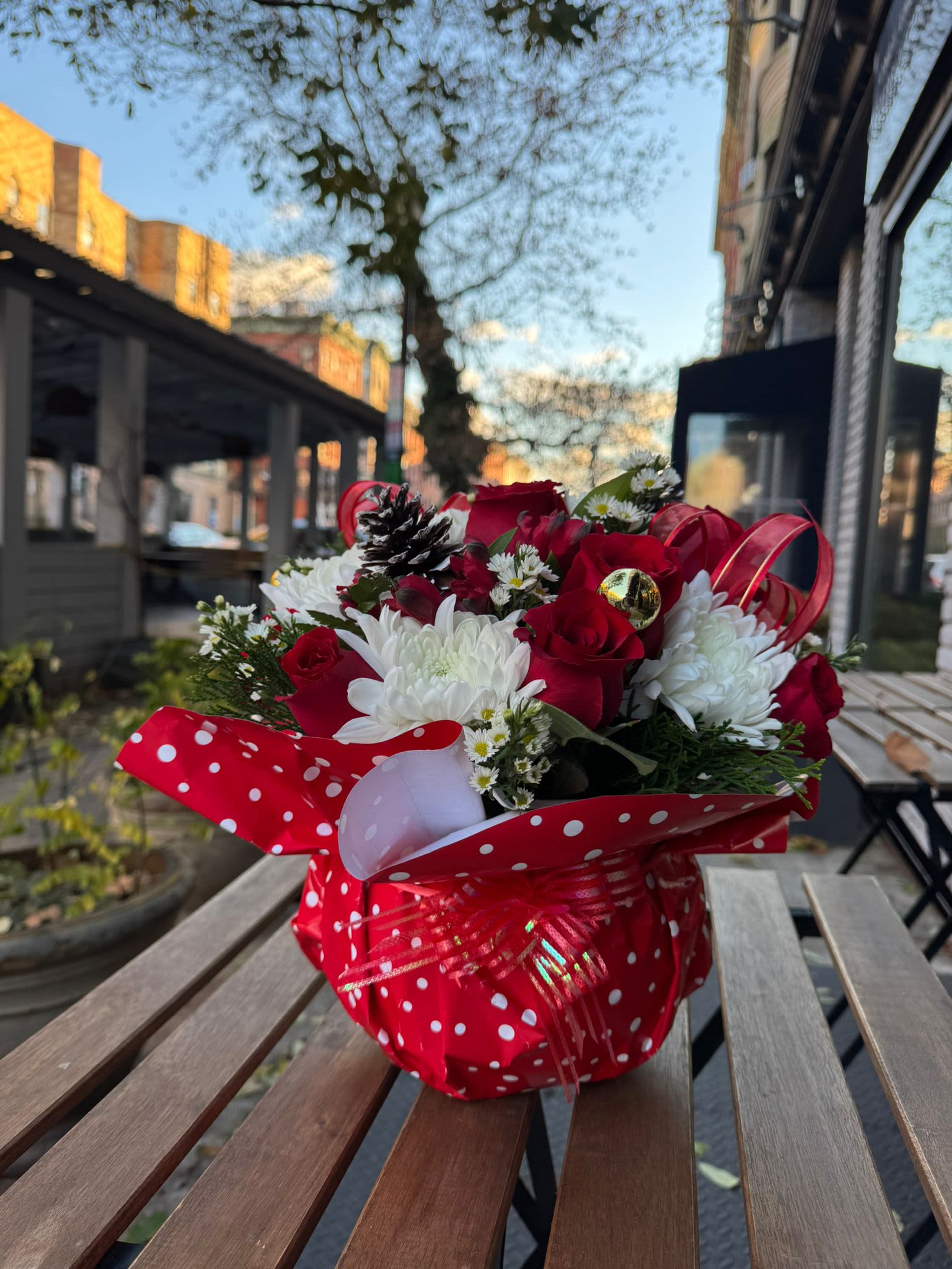 Merry  Christmas - Christmas Centerpiece: Magic and Charm  A design that captures the essence of Christmas, combining fresh flowers, vibrant red tones, classic greens and golden touches. Adorned with festive details such as pine cones, ribbons. This centerpiece is perfect for brightening up your dinners and family gatherings.