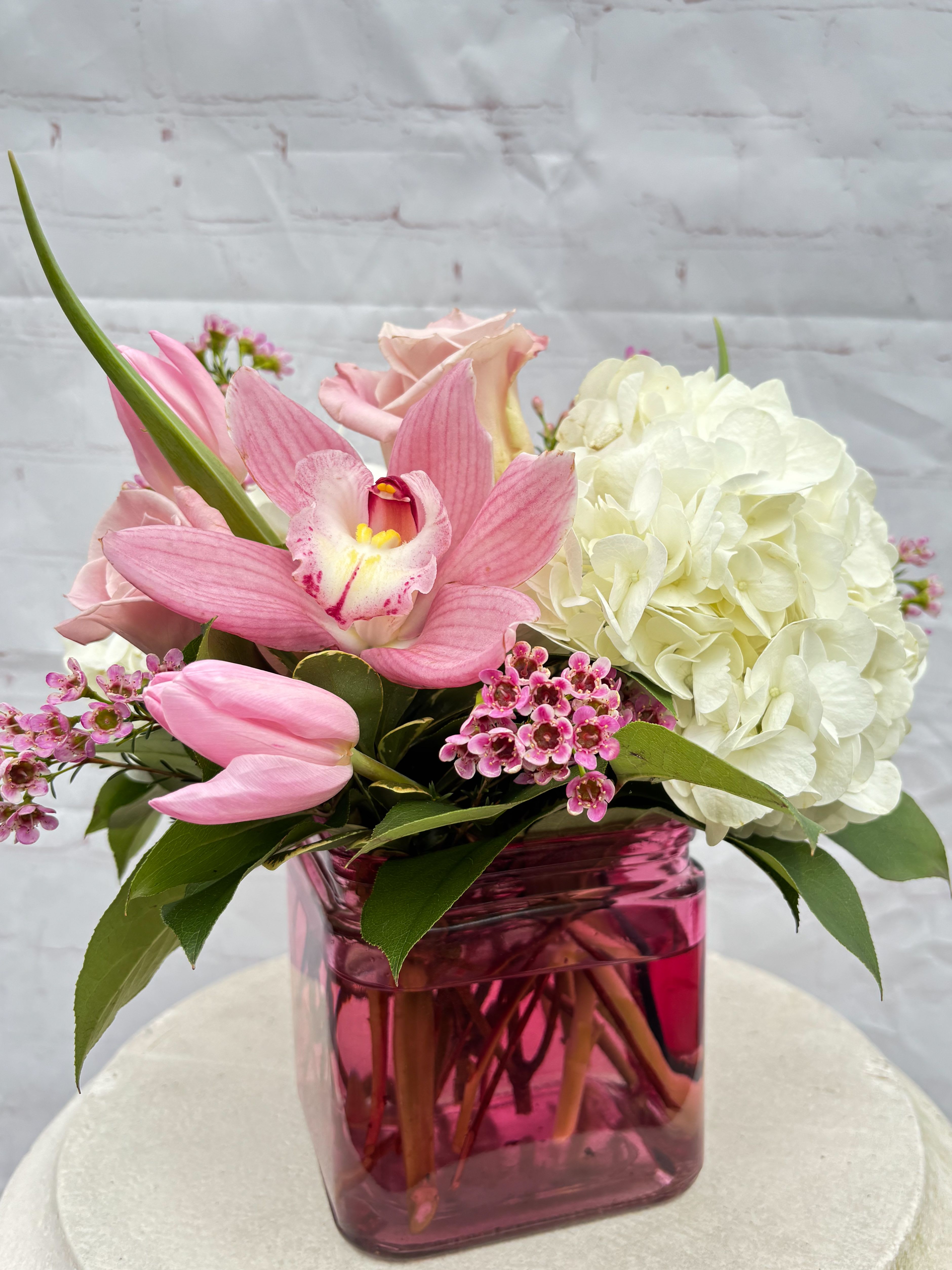Bloom &amp; Blush - This beautiful arrangement contains white hydrangeas, blush pink/whites, blush pink hyacinths, white/blush pink roses, fuchsia colored (cymbidium) orchids, purple wax flower in a unique mauve/pink cubed vase. Please note: flower varieties and colors may vary slightly based on seasonal availability, but the overall look and feel will always remain lush, fresh, and full of love.