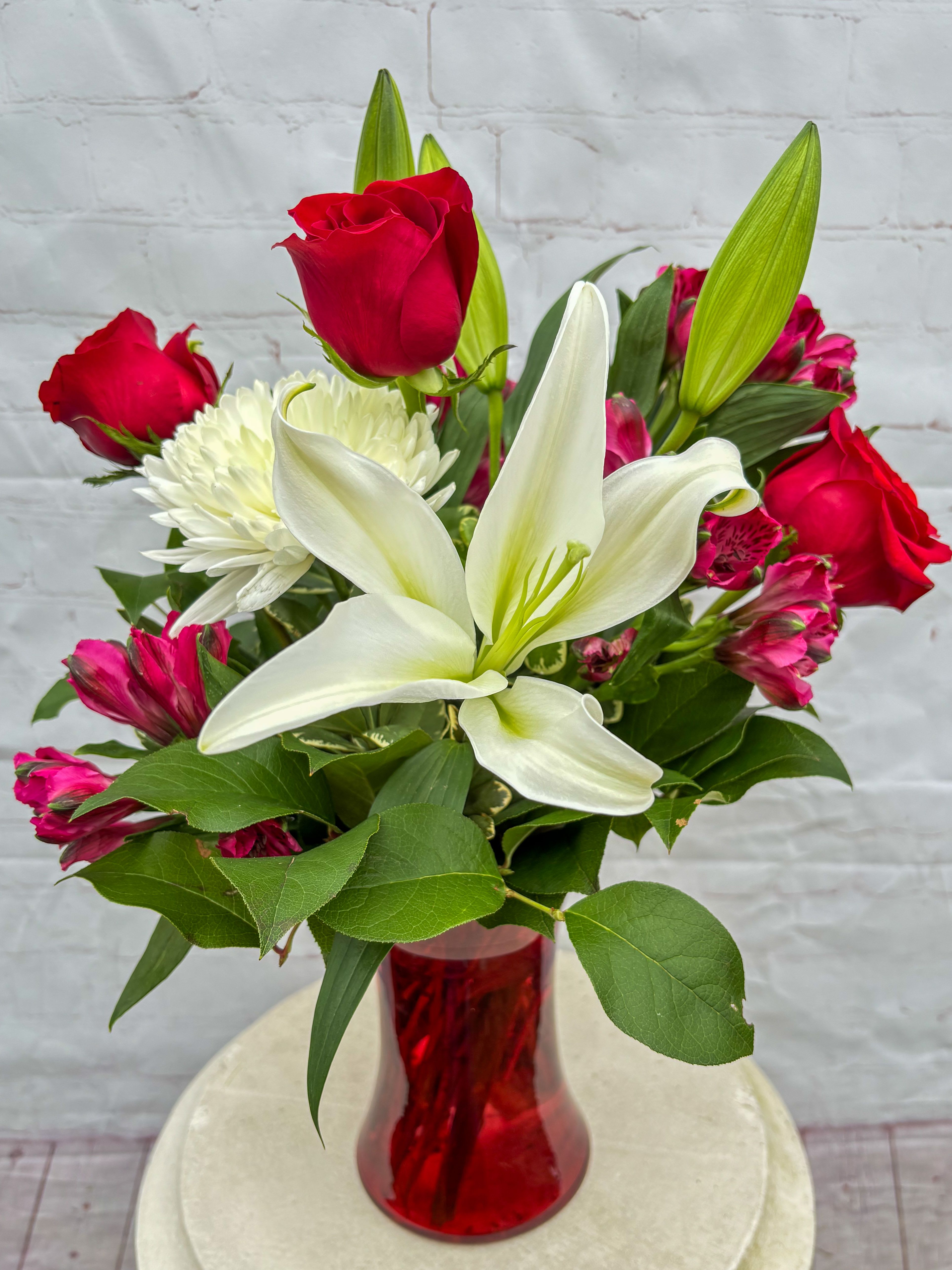 Sweetheart - Sweetheart is a romantic, feel-good arrangement designed to make hearts flutter. Featuring a beautiful mix of roses, lilies, mums, and alstroemeria, this design is artfully arranged in a tall red vase for a bold and elegant presentation. Perfect for celebrating love, admiration, or just because. Please note: flower varieties and colors may vary slightly based on seasonal availability, but the overall look and feel will always remain lush, fresh, and full of love.