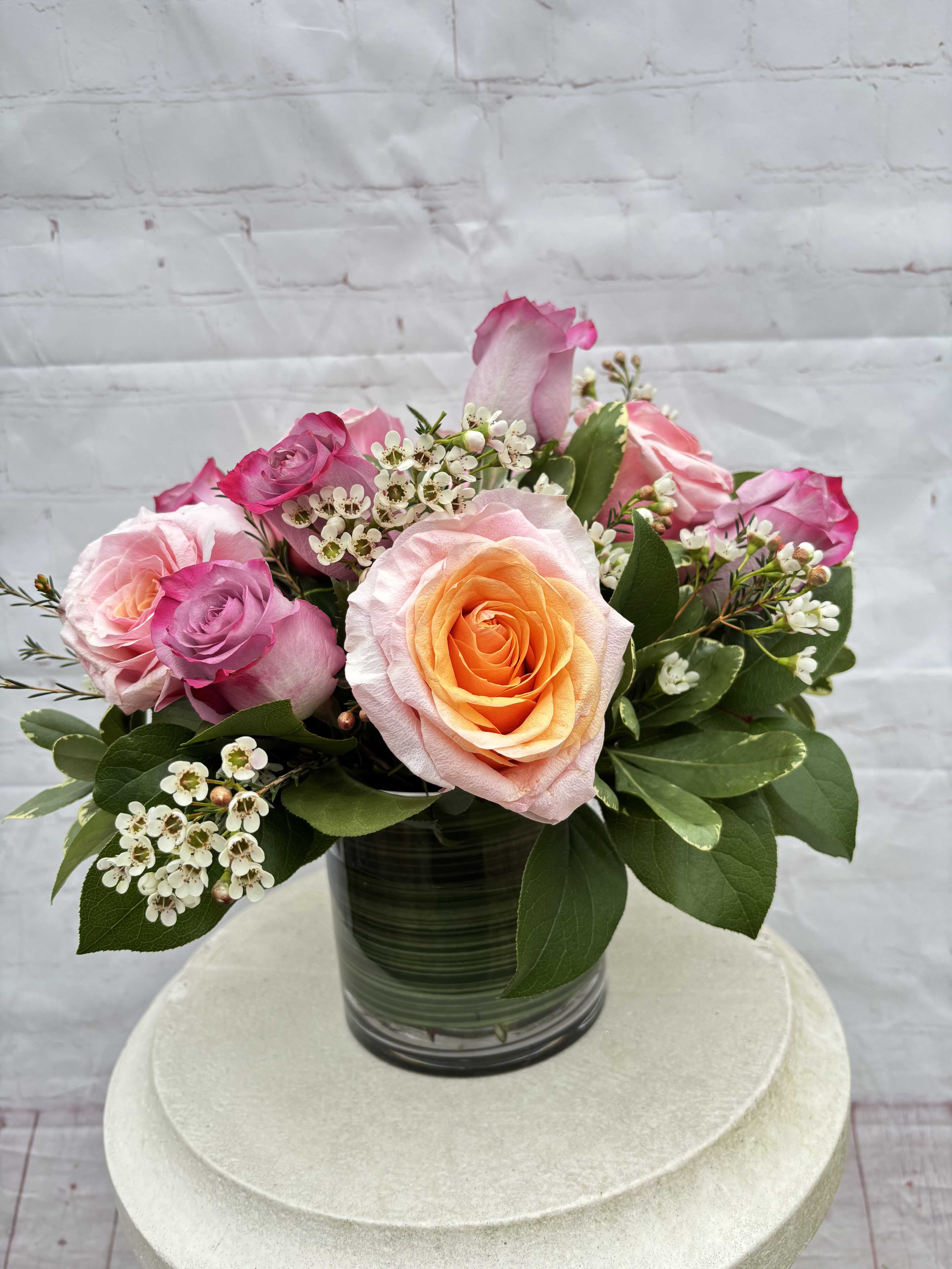 Pink Velvet - Pink Velvet is a low, full arrangement featuring a romantic mix of 12 pink and purple roses, artfully designed to feel soft, lush, and elegant. This timeless bouquet is perfect for celebrating love, friendship, or simply making someone’s day a little more beautiful.  Please note: Flower shades and colors may vary slightly depending on seasonal availability, but the overall look and feel will always remain true to the design.