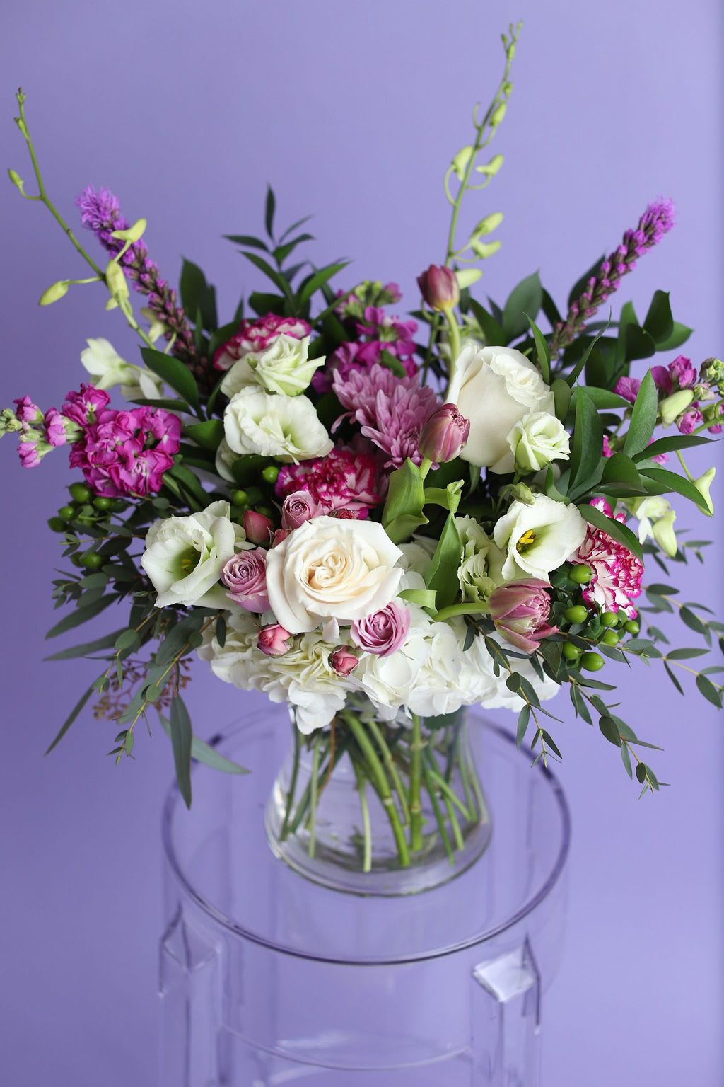 Violet Gardens Grand - Our Violet Gardens Luxe is the elevated, grand version of our beloved cube design — thoughtfully arranged in a premium statement vase for maximum impact. This larger, lush garden-style arrangement features white hydrangea, blush and lavender roses, tulips, ranunculus, lisianthus, and rich violet accents with layered greenery for depth and movement.  Designed for unforgettable moments, this luxury floral centerpiece is perfect for milestone birthdays, anniversaries, romantic gestures, sympathy tributes, and upscale events.  Handcrafted by Bloom-A-Round Floral Design and available for flower delivery in Flower Mound, Southlake, Coppell, Plano, Frisco, Denton, and surrounding DFW areas.  Seasonal substitutions may apply to maintain freshness and overall design style 