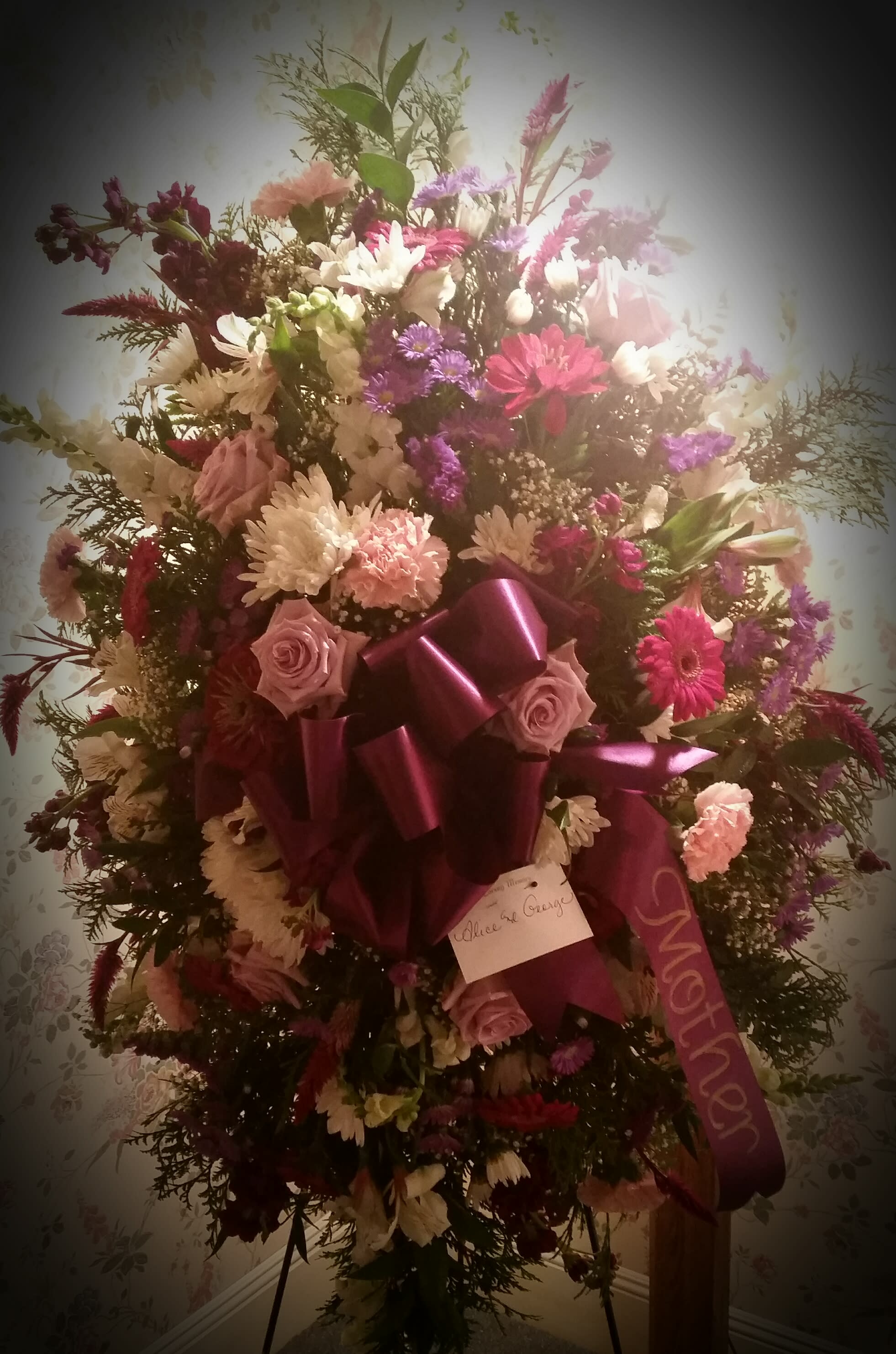 Classic standing spray for funeral - This spray on an easel stands about six feet tall.  A mix of flowers in shades of pink, purple, lavender and white in a garden style arrangement.  A ribbon can be added denoting the deceased's relationship to the sender..