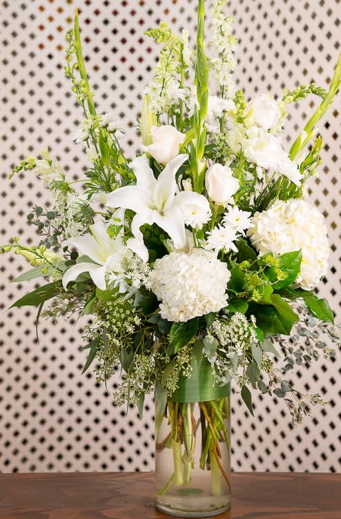 White Wonderland - White hydrangeas, lilies, roses, gladiolas, stock and other white floral in a long glass cylindrical glass vase. 