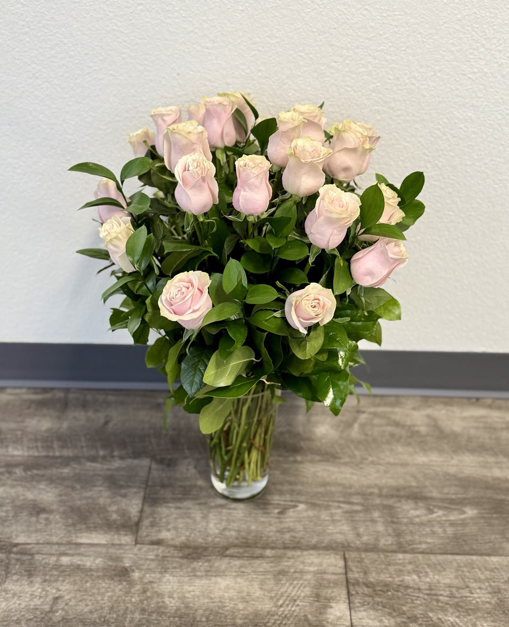2 Dozen Light Pink Roses - A joyful gesture of love and affection, this chic arrangement of light pink roses with fresh greens is a special surprise on any occasion. The light pink roses are arranged with salal and delivered in a clear vase.