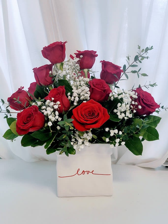 Dozen Red Roses in our 'Love' Ceramic Box - Declare your love with timeless passion – our 'Love' Dozen Red Roses in Ceramic Box is the ultimate expression of romance! This luxurious arrangement features twelve velvety deep red roses in full bloom, artfully paired with clouds of delicate white baby's breath and lush eucalyptus accents for a perfect balance of bold color, soft texture, and subtle fragrance.   Nestled in a chic rectangular white ceramic vase elegantly scripted with 'love' in flowing red cursive, this ready-to-display masterpiece arrives fresh and thoughtfully designed to wow. The classic red roses symbolize deep love and desire, while the airy baby's breath adds purity and the eucalyptus brings a touch of modern sophistication—creating a stunning centerpiece.   Ideal for Valentine's Day surprises, anniversaries, birthdays, or simply saying 'I love you' in the most beautiful way. Limited seasonal availability—order now and make their heart skip a beat with this enduring symbol of devotion!