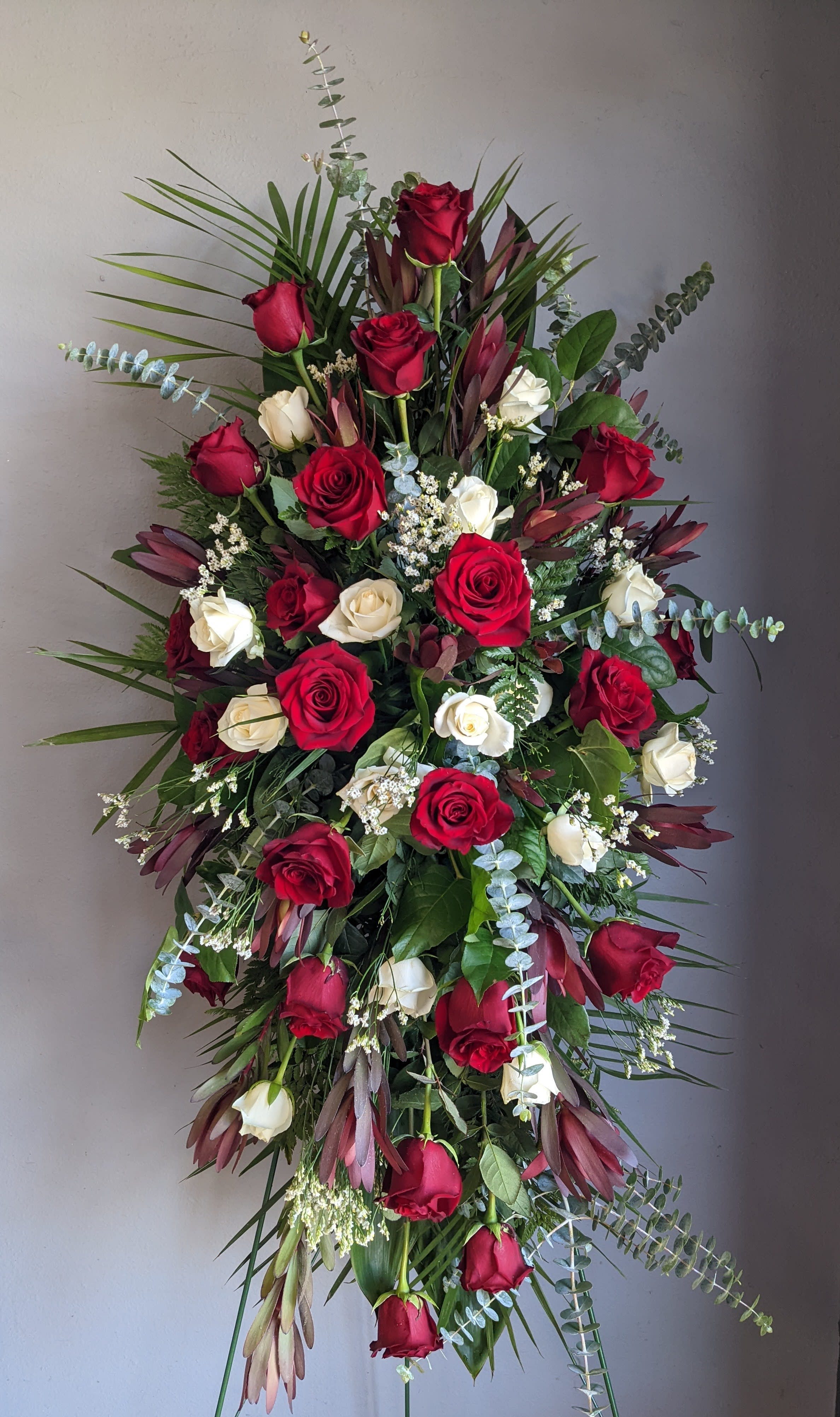 FUNERAL STANDING SPRAY - Rose Elegance 35 - This is a wonderful option for a funeral service, church or graveside . This standing spray is a one sided flower arrangement on a 5' easel (easel included). This elegant mix of red and white flowers of roses, protea and greenery is a stunning option to remember you loved one in flowers.  **This is a piece for a funeral or memorial service. Please place the order at least 2 days prior to the service to guarantee a certain arrangement. Anything sooner and we cannot guarantee it will match the picture. These pieces can be customized to the color of your choice. The flowers may vary depending on availability of the flowers, special requests and quality of the flowers we have in stock. If you have a special request please add it to our special instructions when placing your order. If you have any questions please don’t hesitate to call. 714 289 1123**