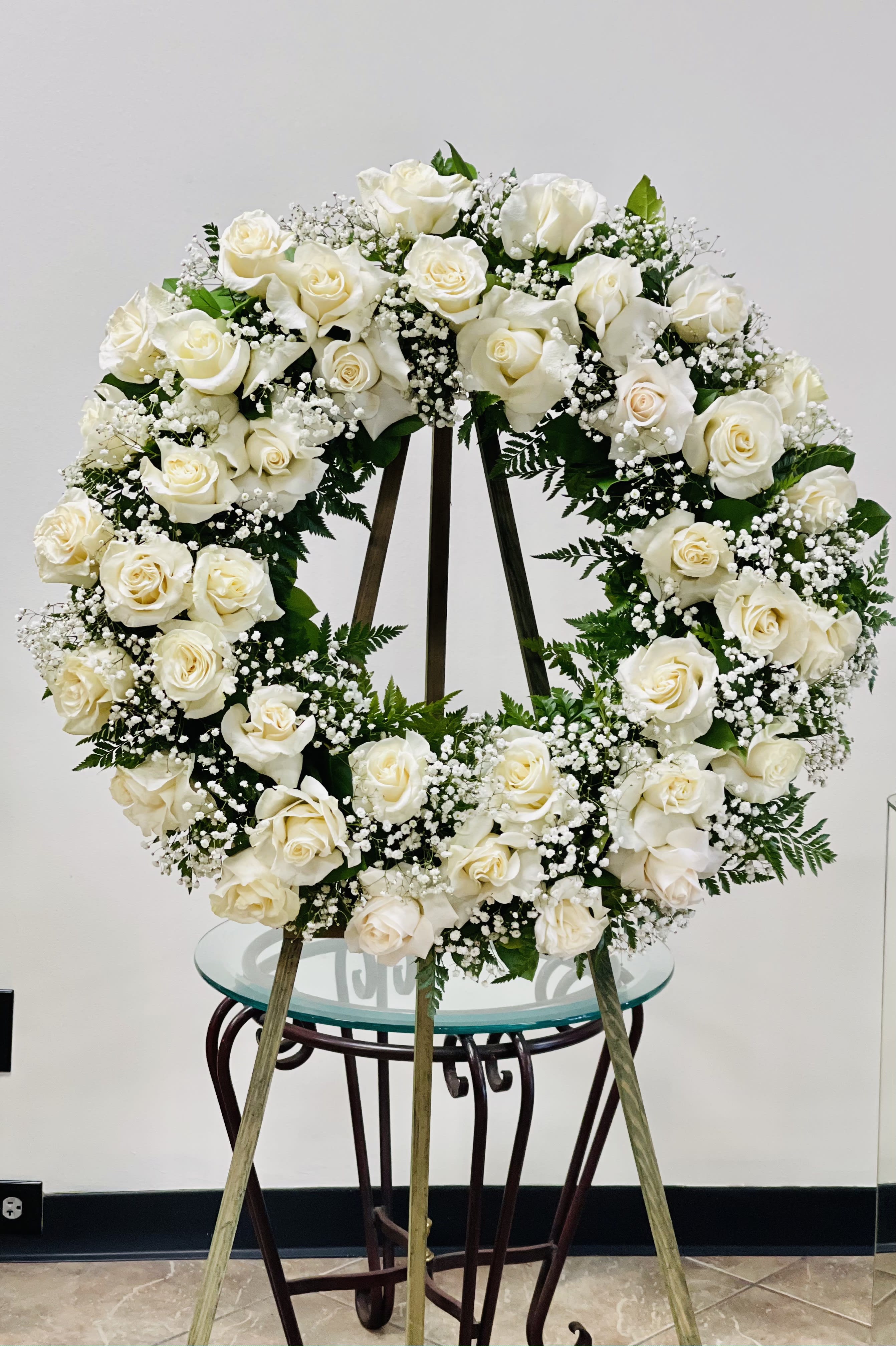 BF-SRW1 Wreath - A sympathy wreath of profound elegance, this creation is a heartfelt tribute adorned with white ecudorian roses and delicate white baby's breath. Measuring a substantial 26 inches in width, the wreath is a visual embodiment of compassion and remembrance, designed to offer solace during a time of loss