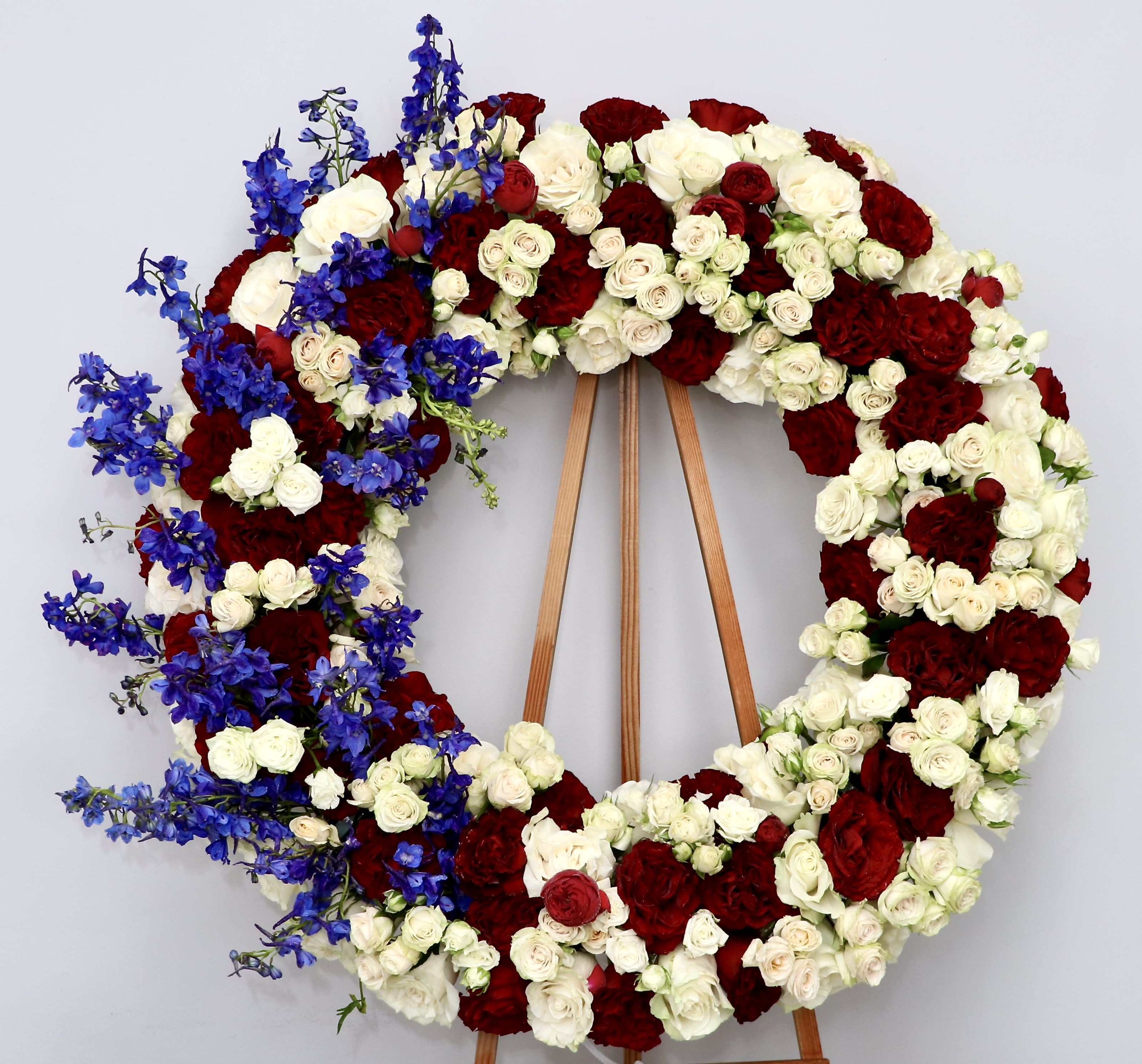 Patriotic Wreath  - This wreath includes seasonal, reds, whites and blue flowers.     We include easel, printed banner and delivery (some fees may apply). An additional banner can be added for $15    Standard size is 30'', deluxe is 36'', and premium is 42''.