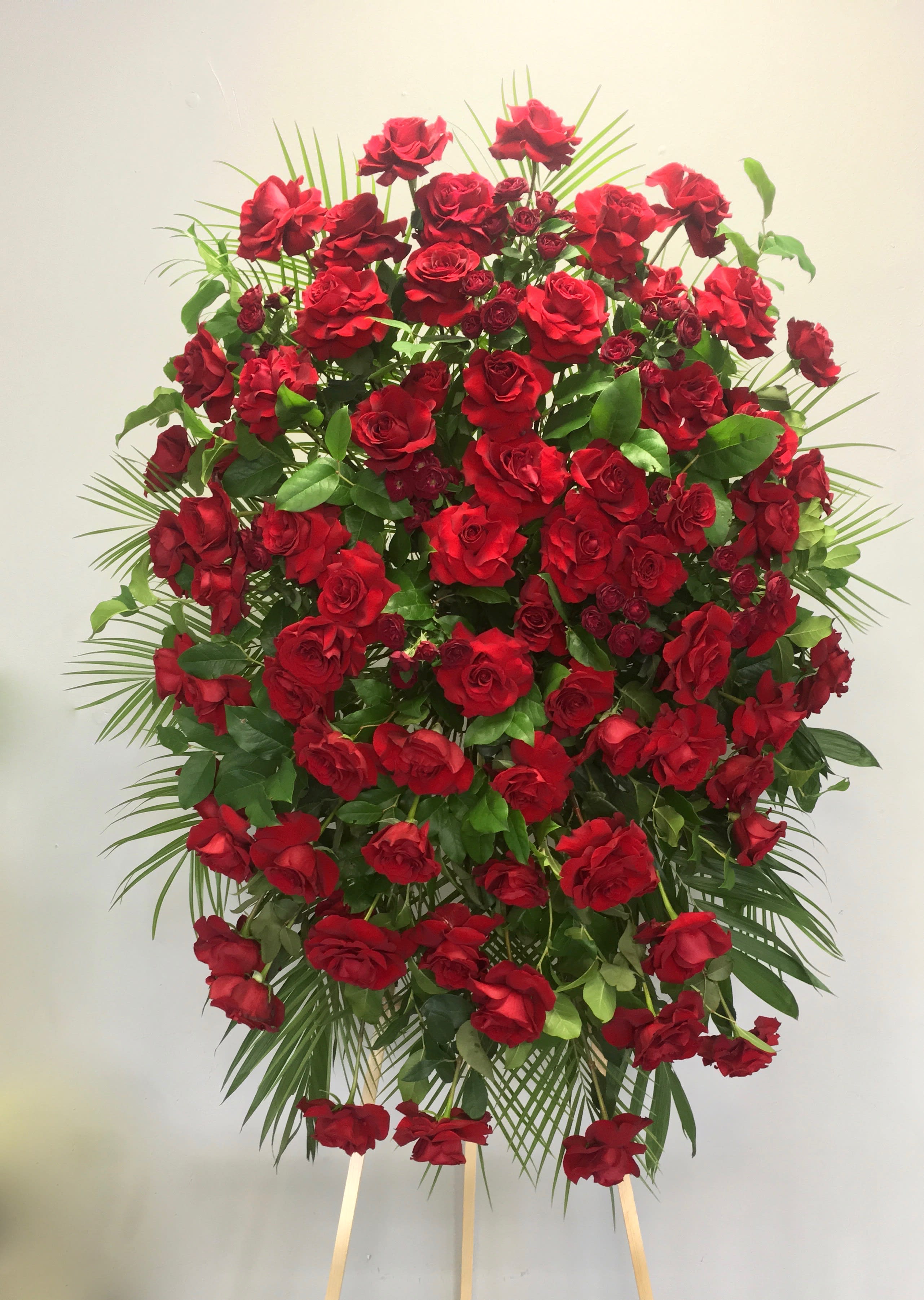 Red Rose Spray - Simple and elegant, this sympathy spray features red roses surrounded by seasonal greens.     We include easel, printed banner and delivery (some fees may apply).    Standard size is 30'' wide, deluxe is 36'', and premium is 42''.