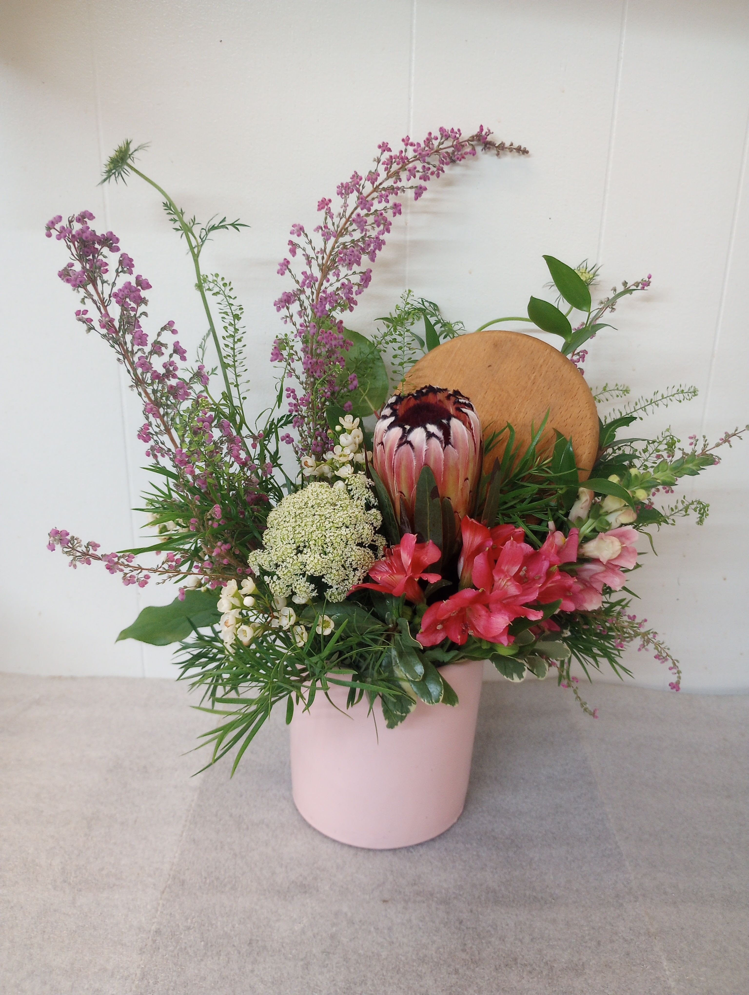 Keepsake  - A 6"x6" canister with a wooden lid is filled with a pink protea, alstromeria and heather.The  keepsake canister that can be kept for later. 