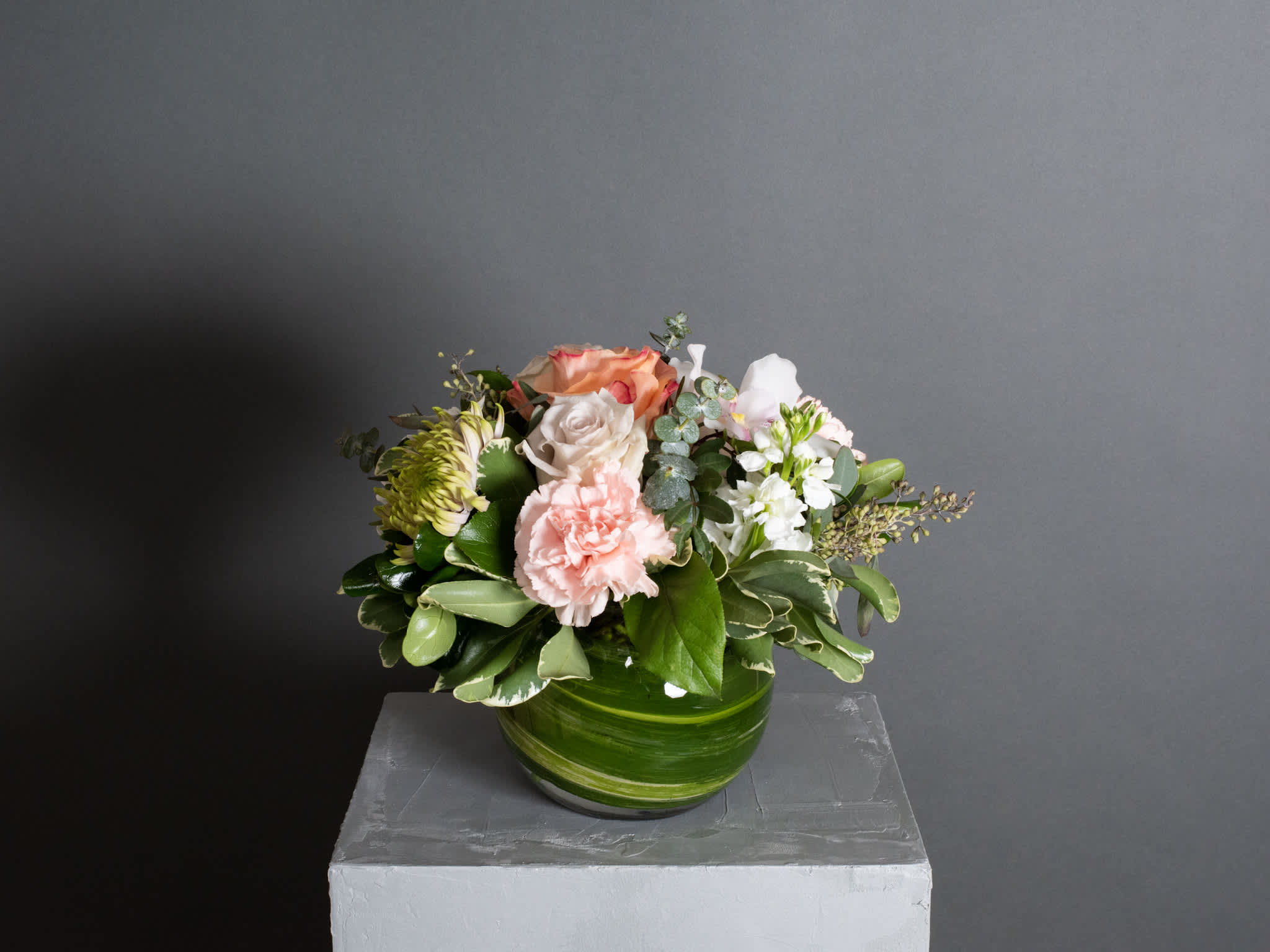 Petite Monet - Bubble Vase Arrangement - The "Petite Monet" is a delicate and airy display of blush-toned blooms. This charming design features carnations, chrysanthemums, cymbidium orchids, stock, and roses, all complemented by seasonal greenery. Arranged in a bubble vase, it offers a graceful touch to any space. Vase size : 6"DX5"H